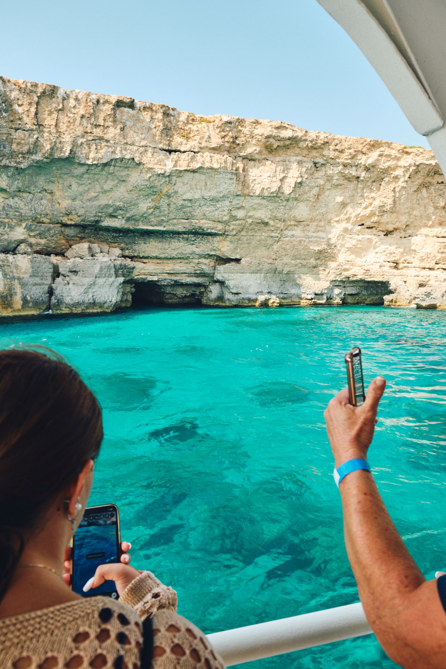 Tourist capturing photos of stunning blue waters and limestone cliffs in Malta's Blue Grotto.
