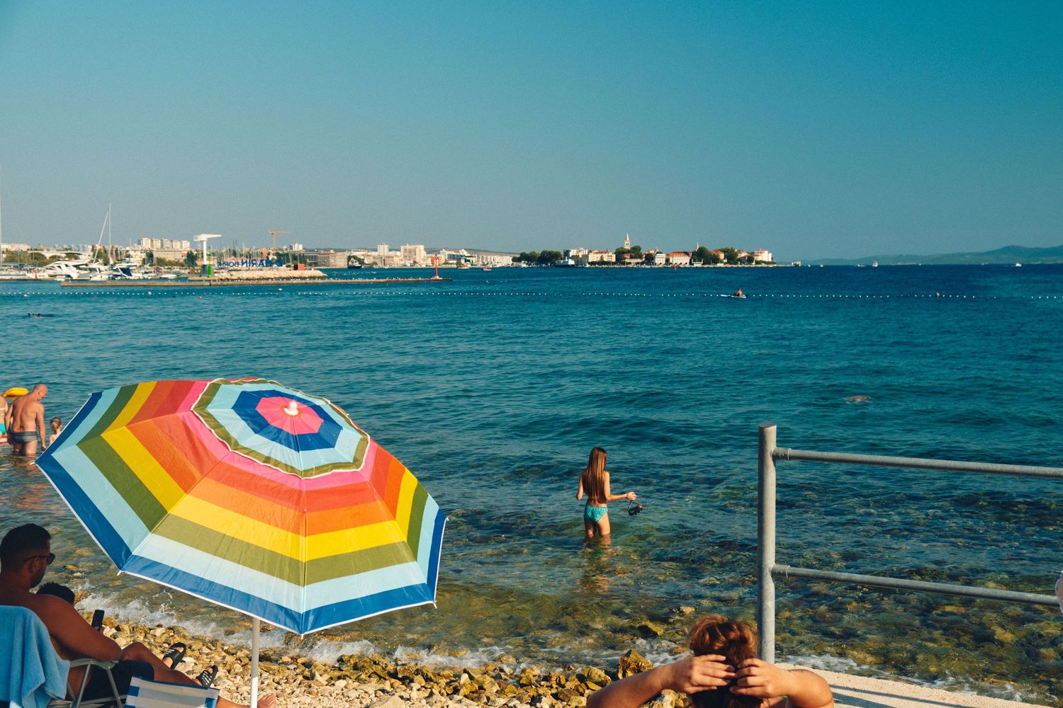 Colorful striped beach umbrella by blue Mediterranean waters.