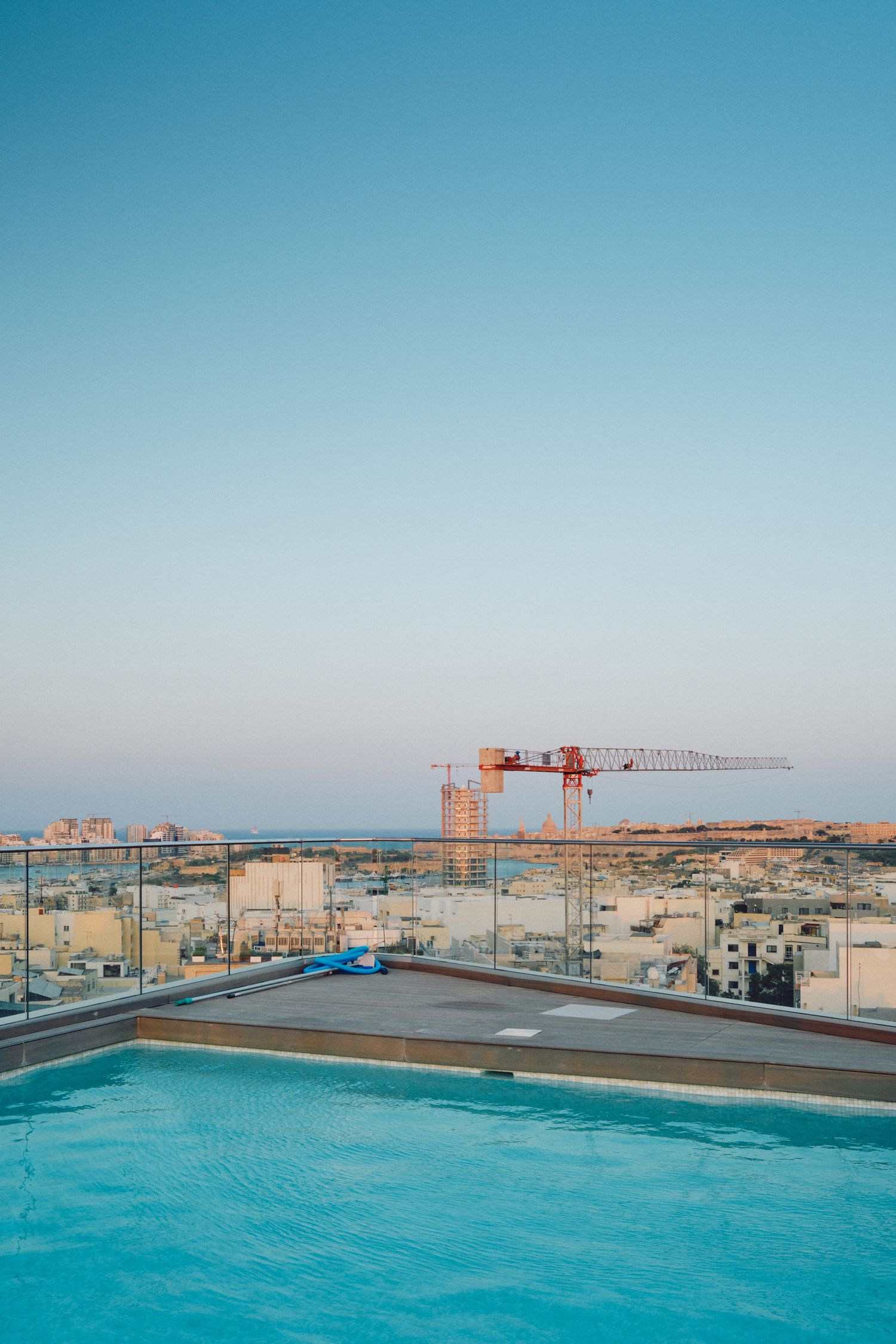 Modern rooftop swimming pool with construction cranes visible against blue sky.