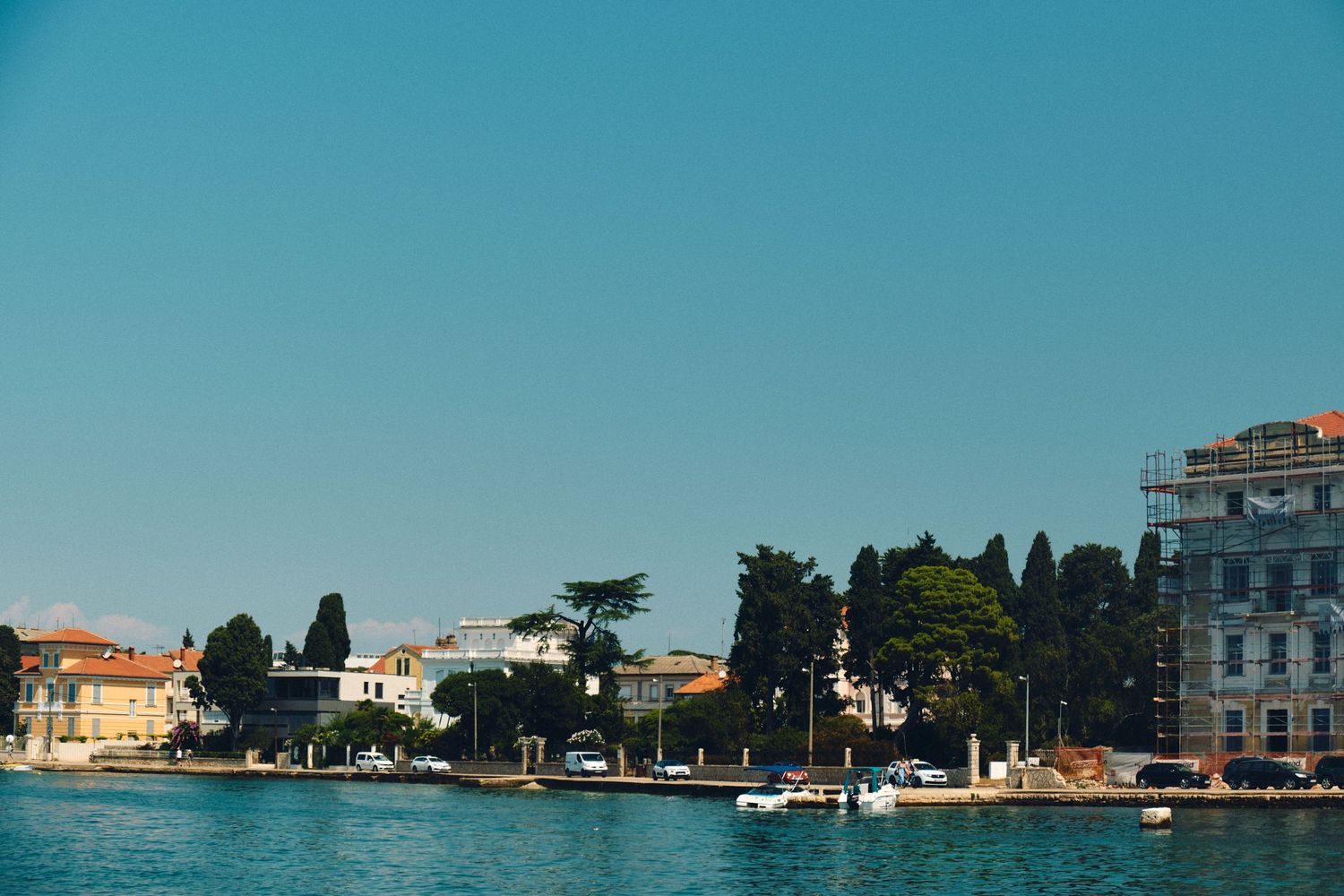 Scenic waterfront view of coastal buildings and trees along calm blue waters.