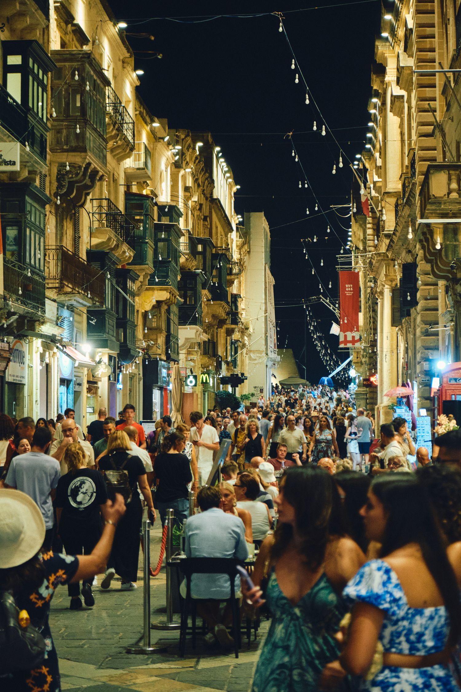 Bustling nightlife street in Malta with string lights and historic buildings.