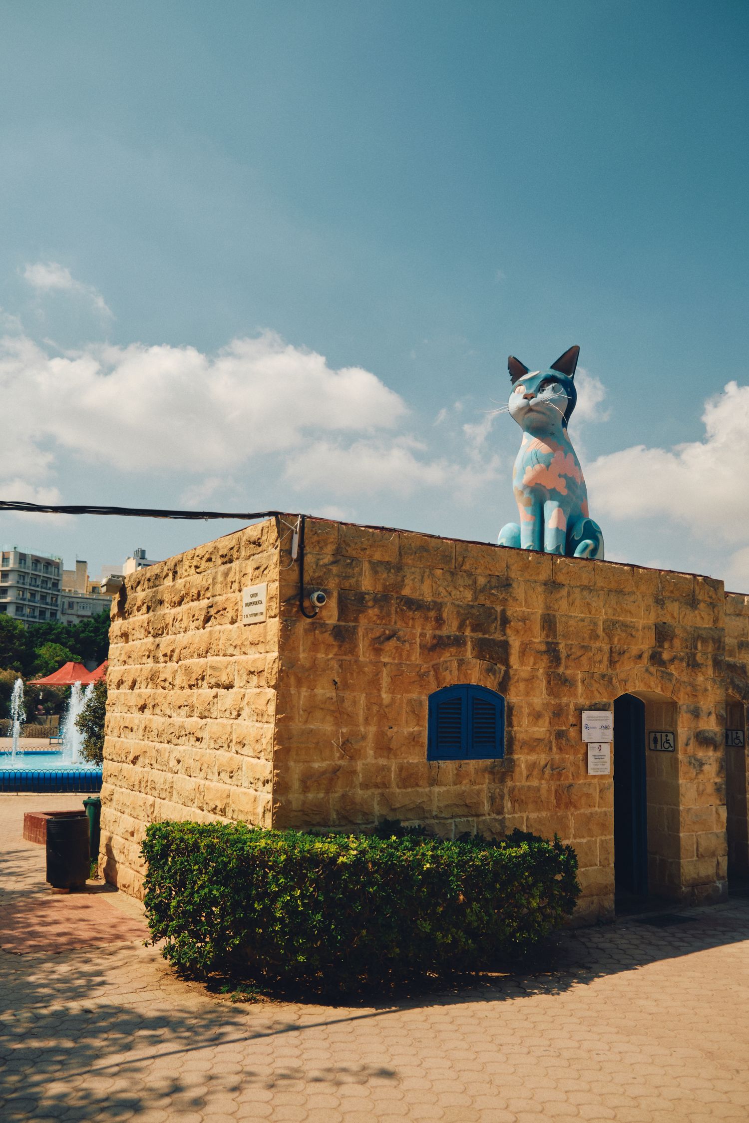 Large blue cat sculpture displayed on top of a sandstone building against cloudy sky in Malta.