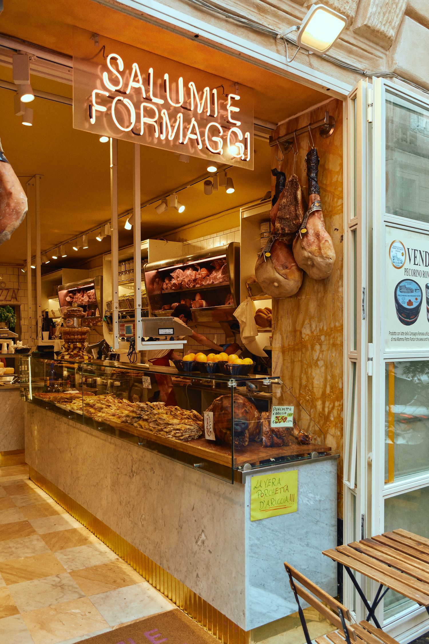 Italian delicatessen storefront with neon 'Salumi e Formaggi' sign and cured meats on display.