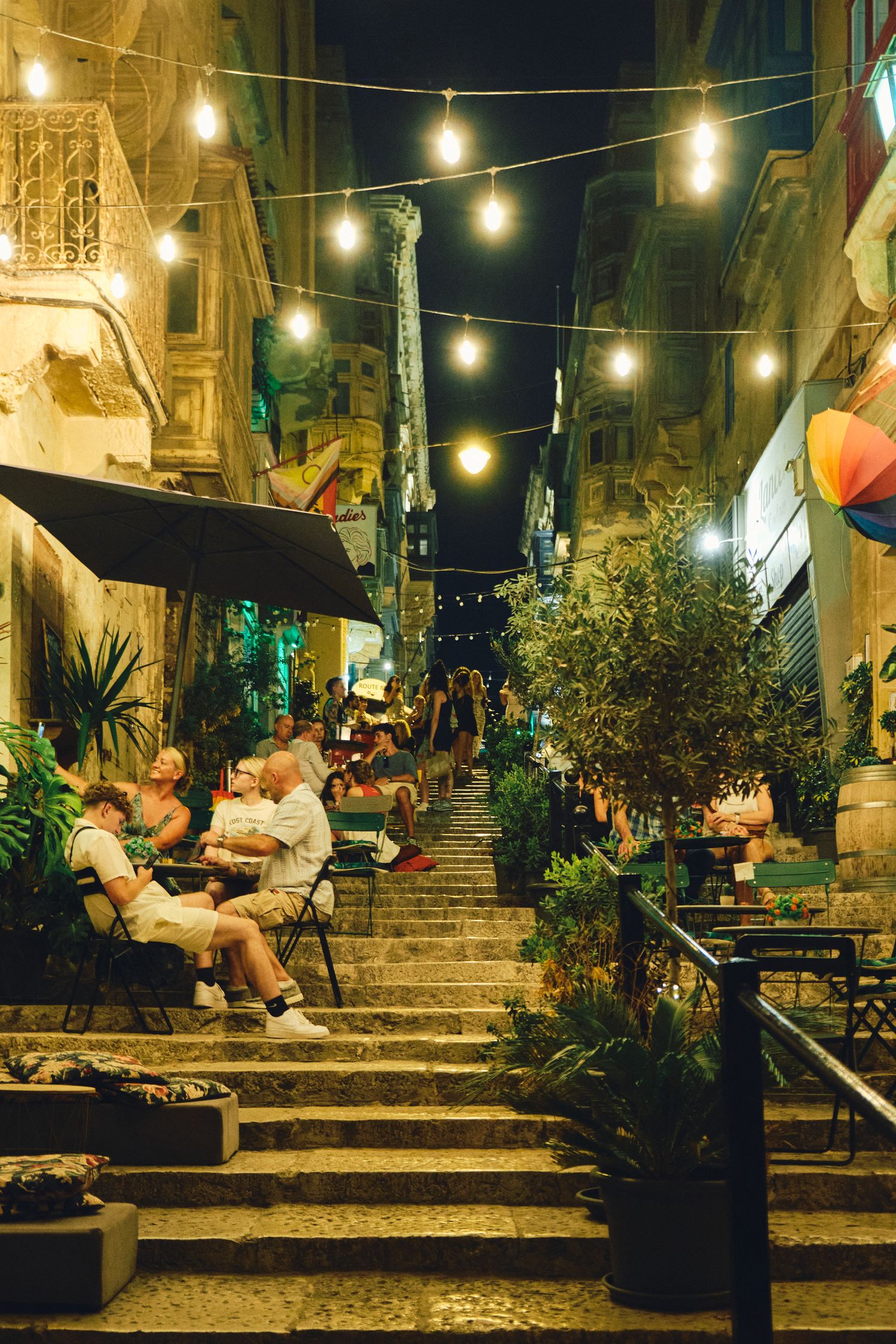 Stone steps adorned with string lights and potted plants create an inviting evening dining atmosphere.