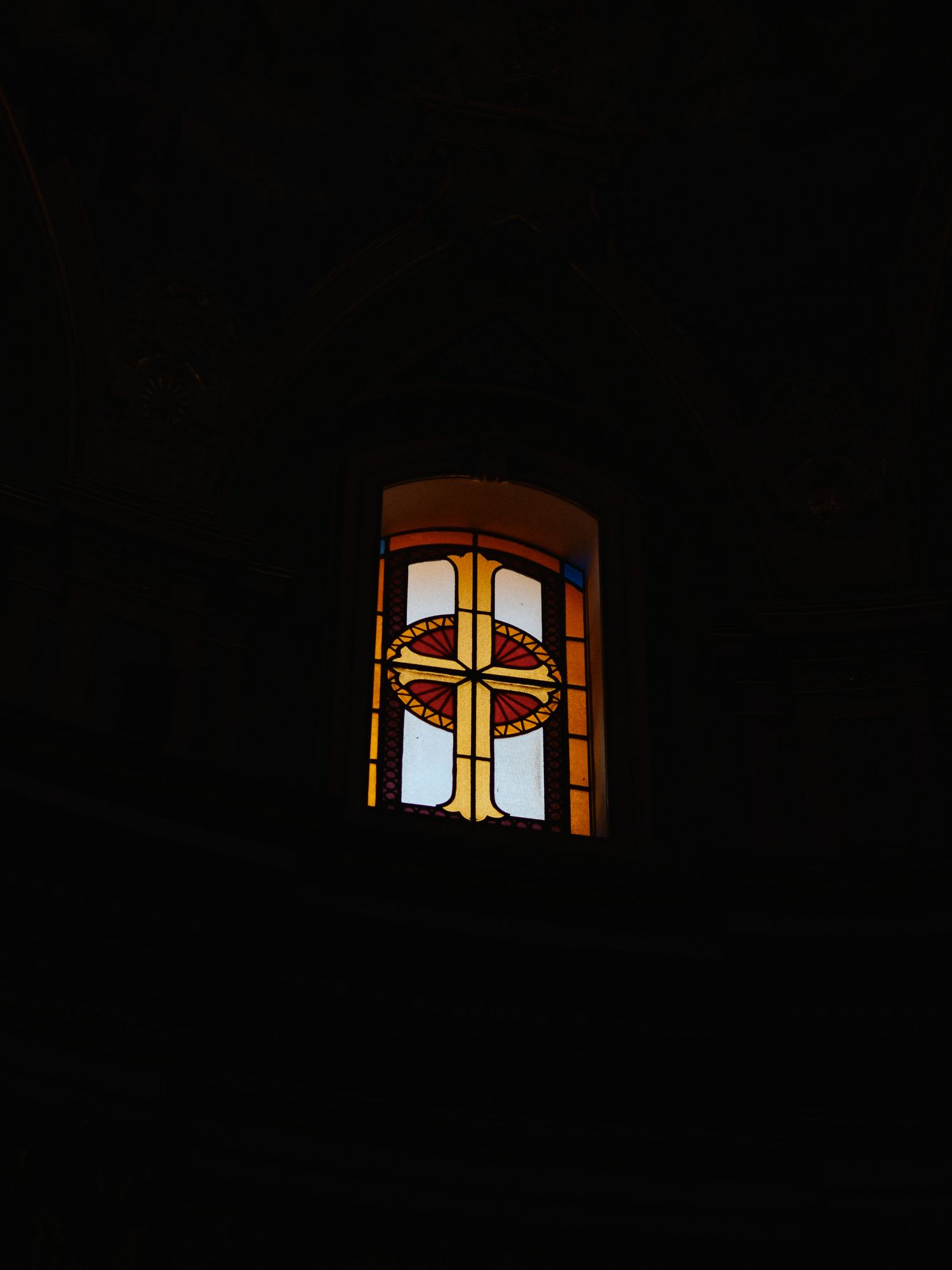 Church window with illuminated stained glass cross pattern at night.
