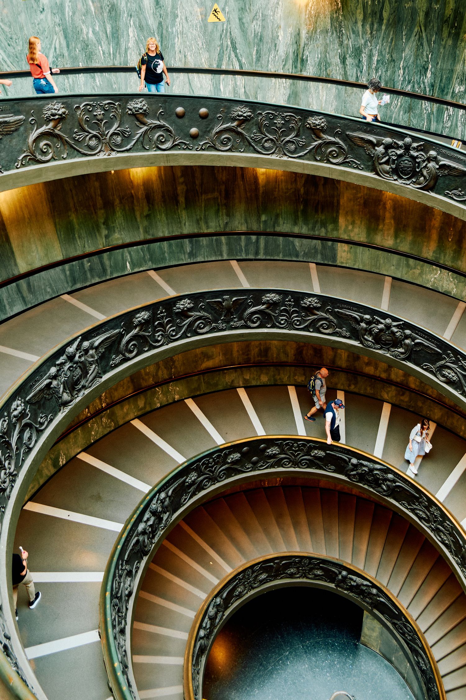 Dramatic spiral staircase with ornate railings and visitors walking down the steps.