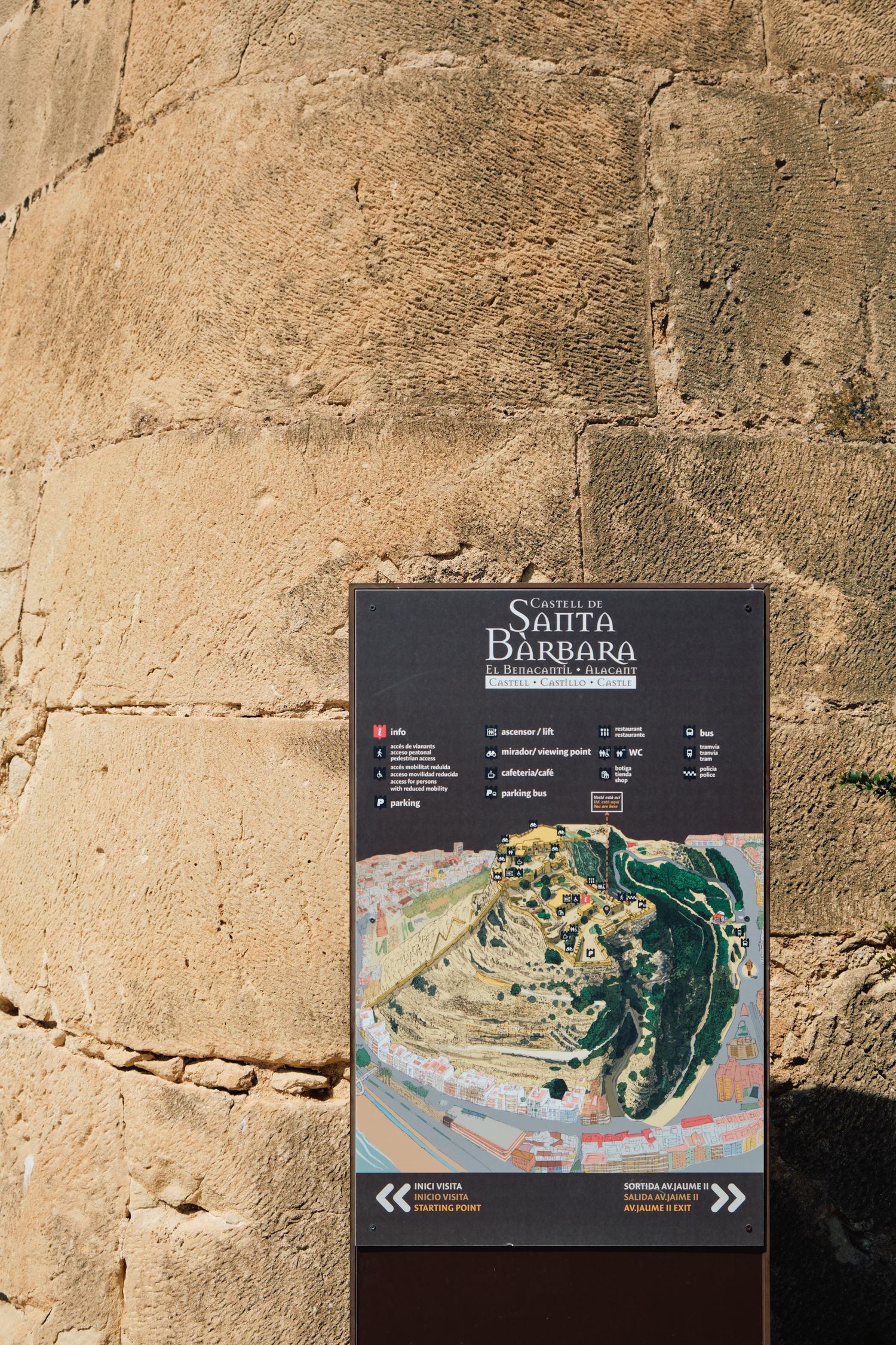 Information sign showing a map of Santa Barbara castle and fortress against a stone wall background.