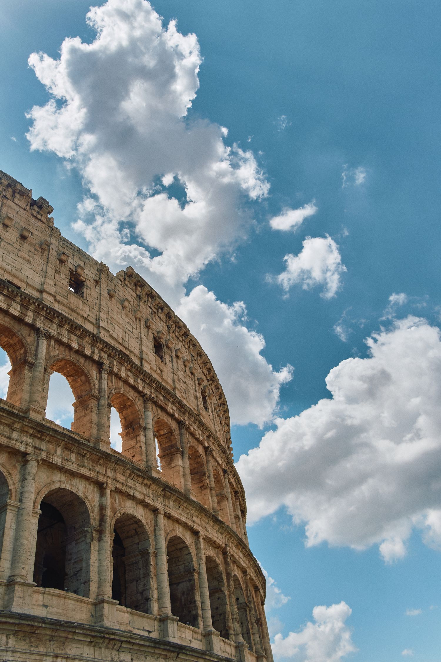 Dramatic upward view of the Colosseum's arched facade against a cloudy blue sky in Rome.