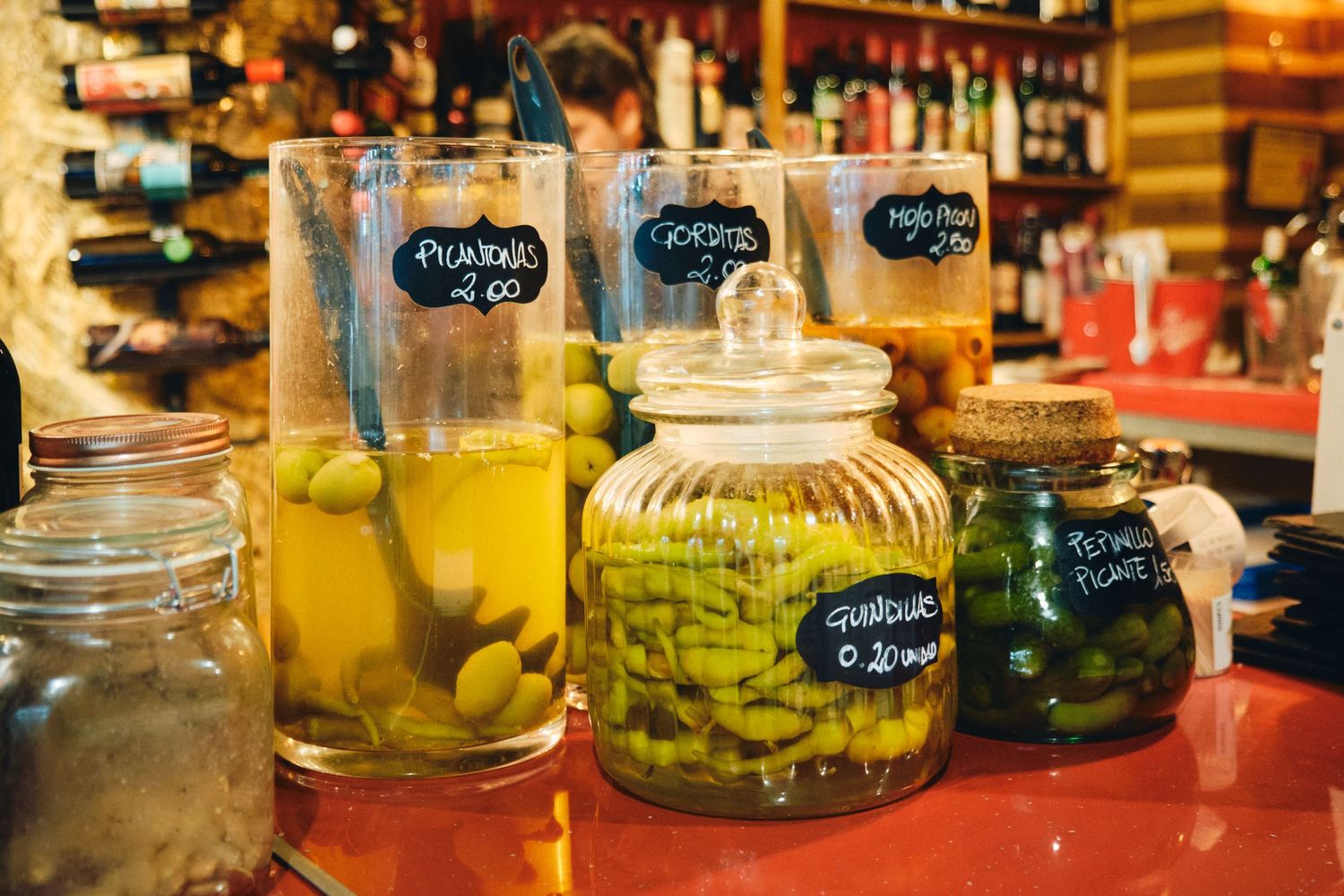 Large mason jars containing various pickled vegetables with handwritten labels on display.