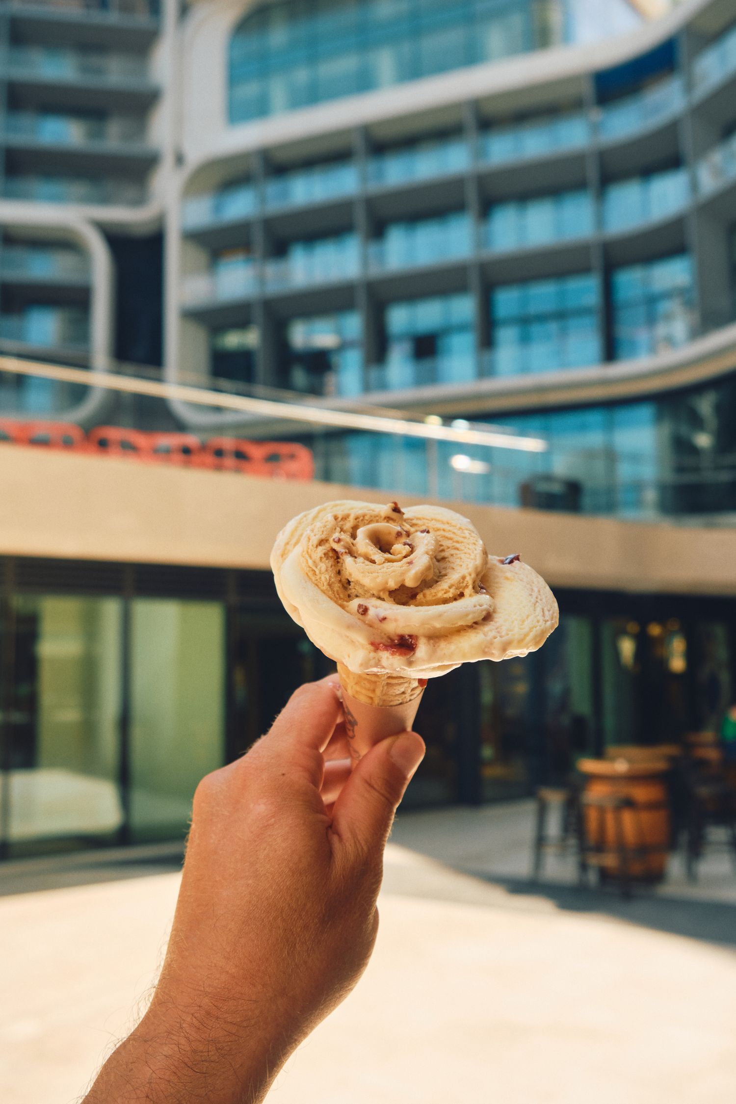 Hand holding a rose shaped ice cream in front of a modern glass building.