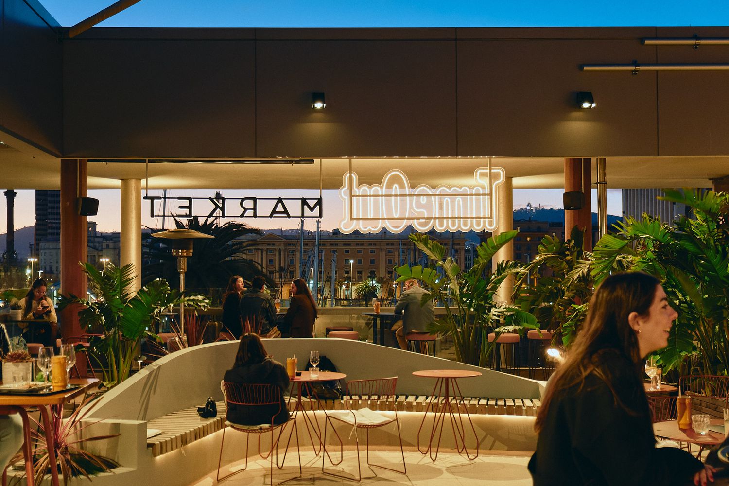 Rooftop bar and restaurant with lush tropical plants, modern seating, and glowing Market sign at dusk.
