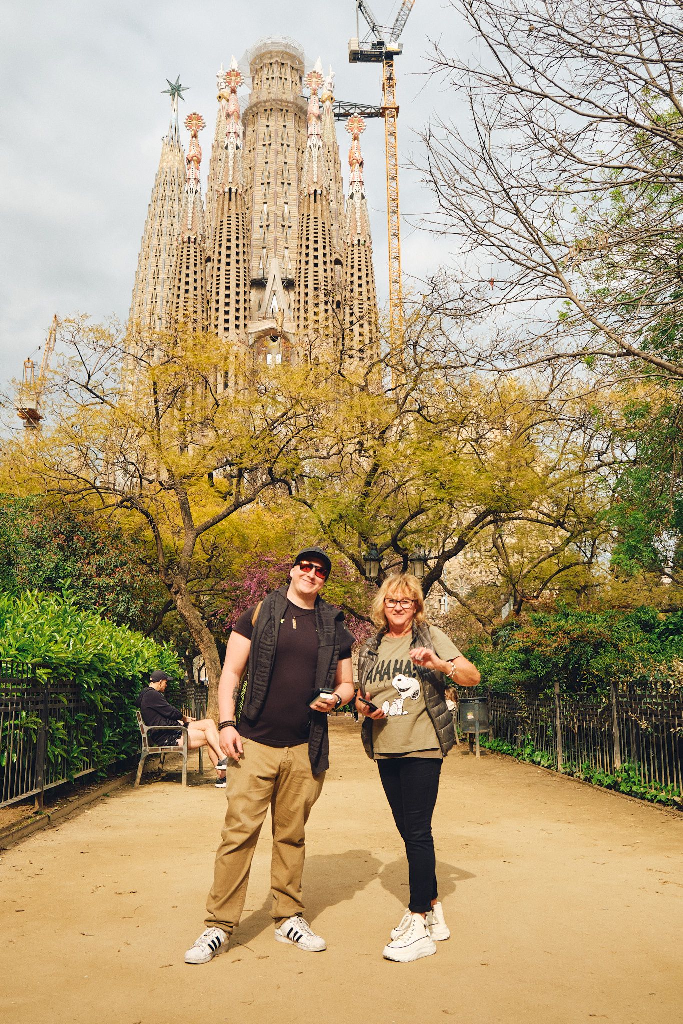 Couple posing in front of Sagrada Familia basilica in Barcelona, Spain, surrounded by autumn trees.