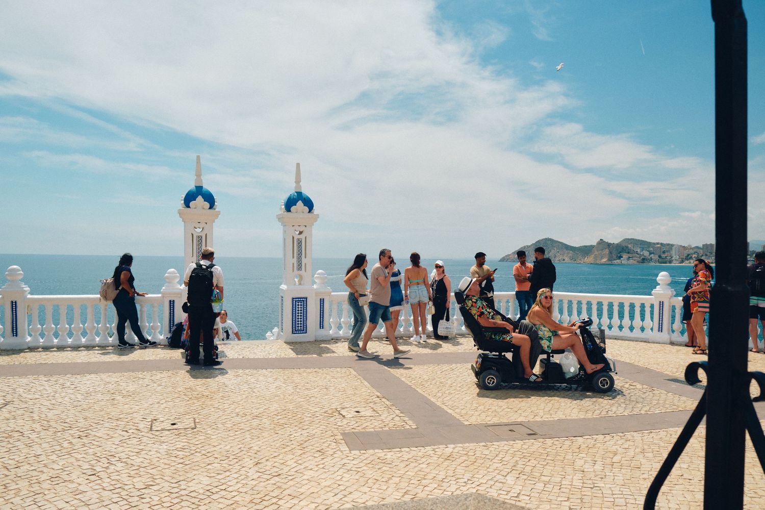 White decorative balcony overlooking the Mediterranean Sea with tourists enjoying the viewpoint.