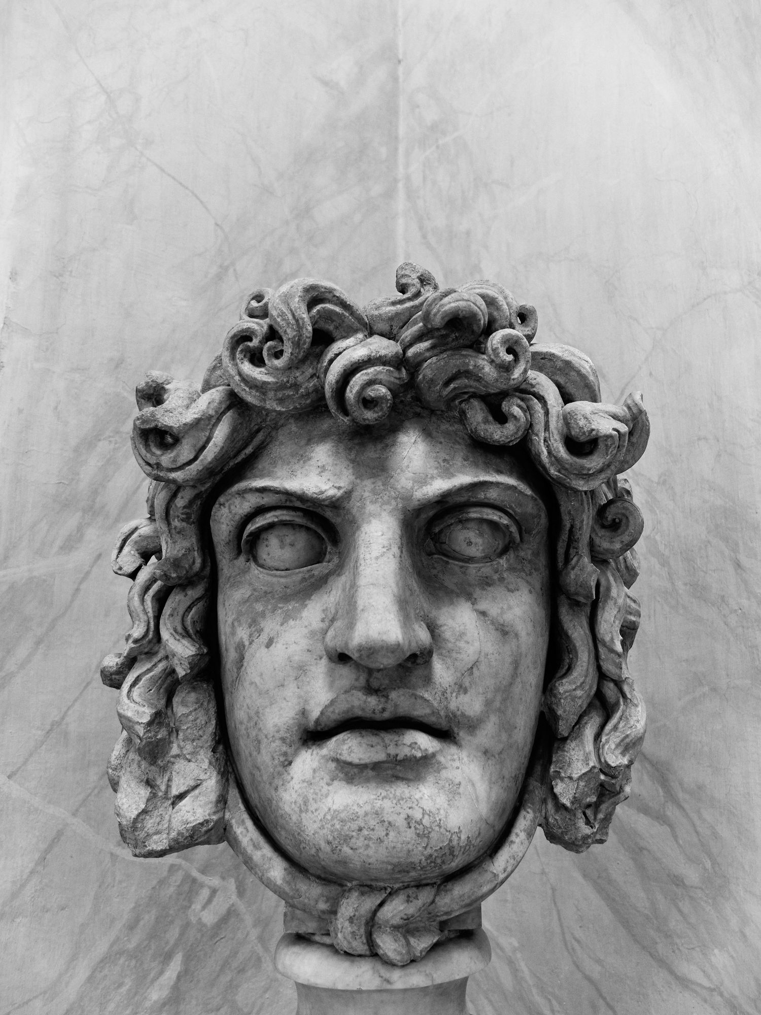 Classical stone sculpture of a face with curly hair in black and white.