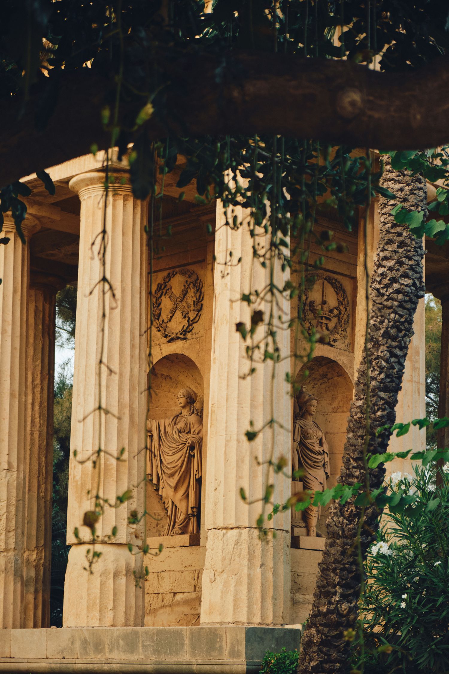 Classical stone columns with religious statues and ornate carvings framed by green foliage.