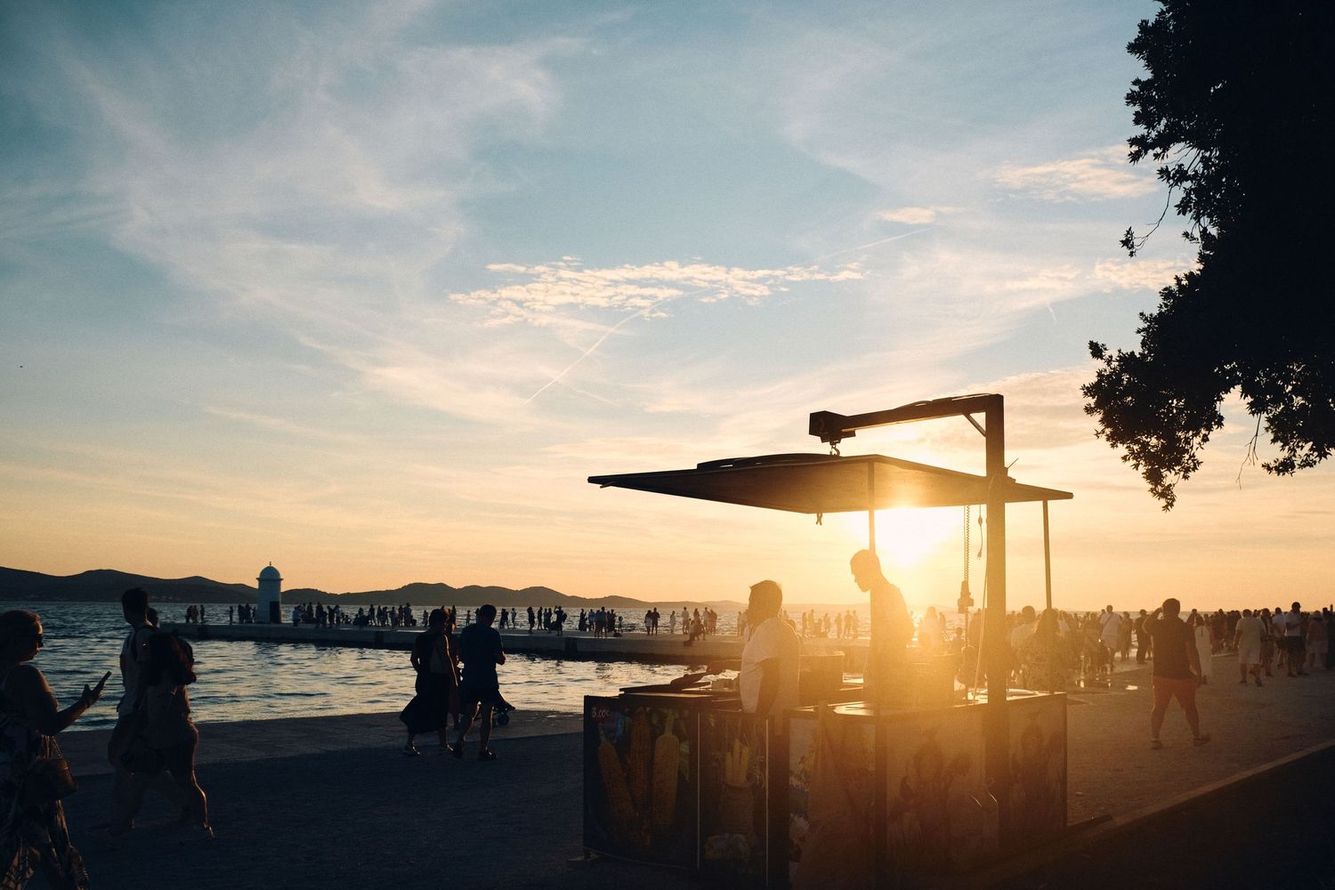 Outdoor beachfront scene at golden sunset with silhouettes of visitors and structures.