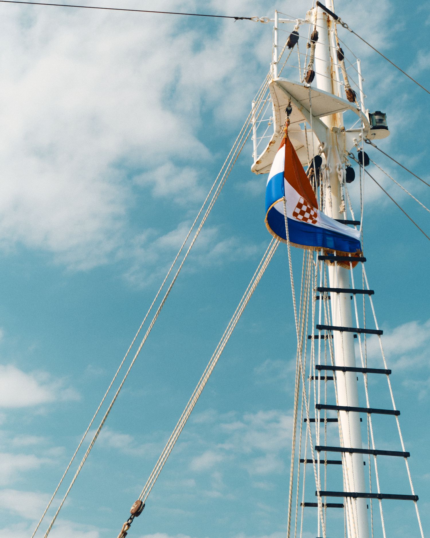 Ship's mast with Croatian flag against blue sky with white clouds.