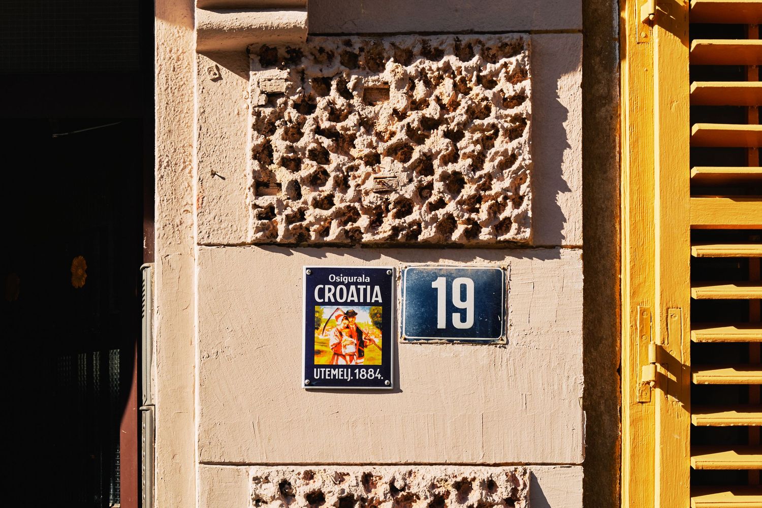 Stone wall detail with decorative pattern and house number 19 sign in Croatia.