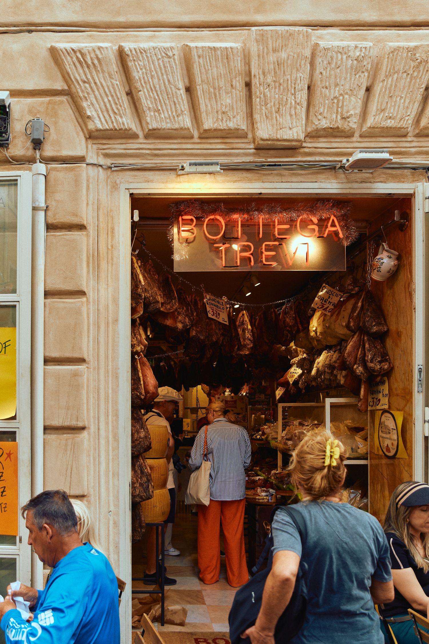 Traditional Italian food shop with neon 'Bottega Tre' sign and hanging cured meats.