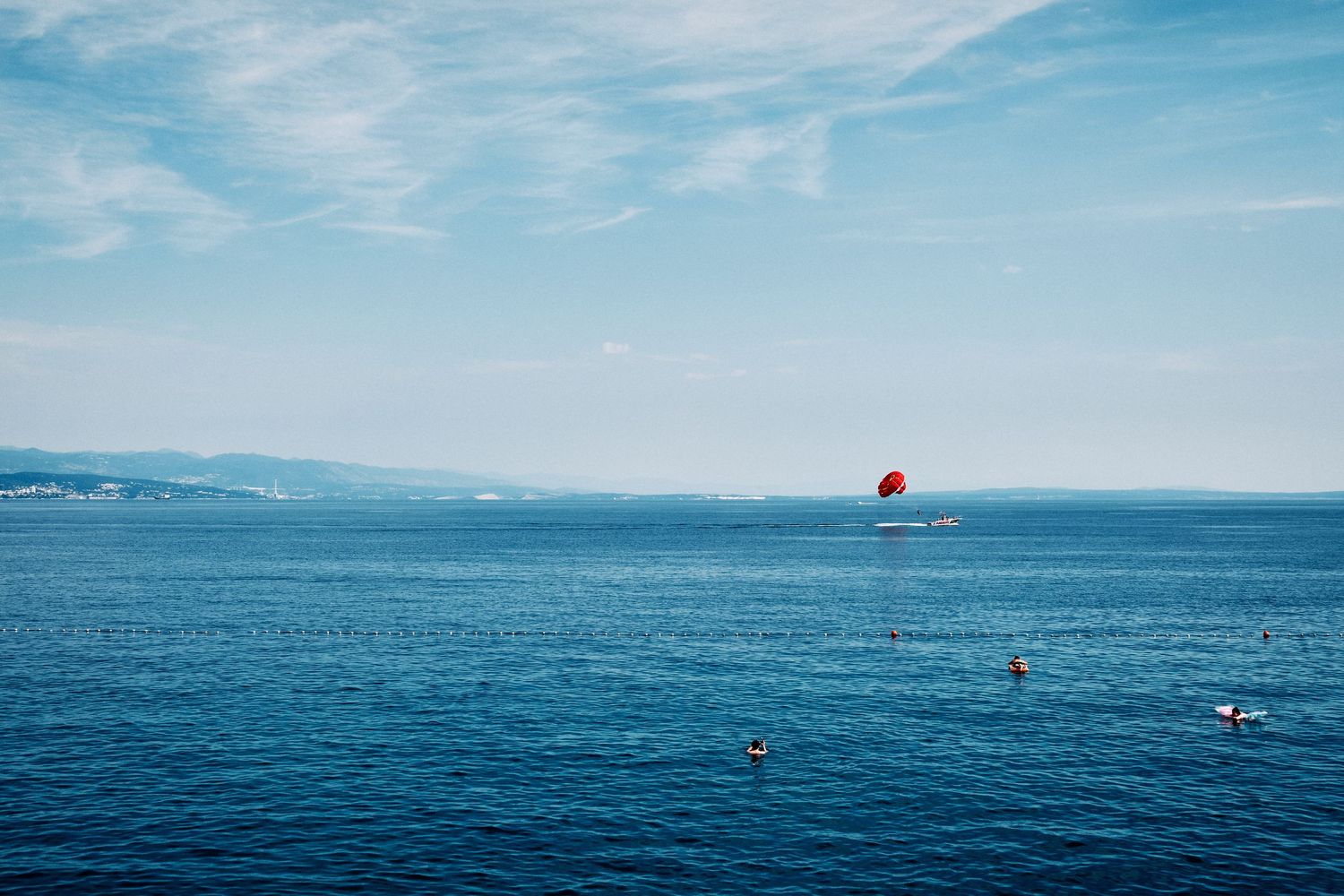Blue ocean waters with distant red parasail and coastal mountains in background.