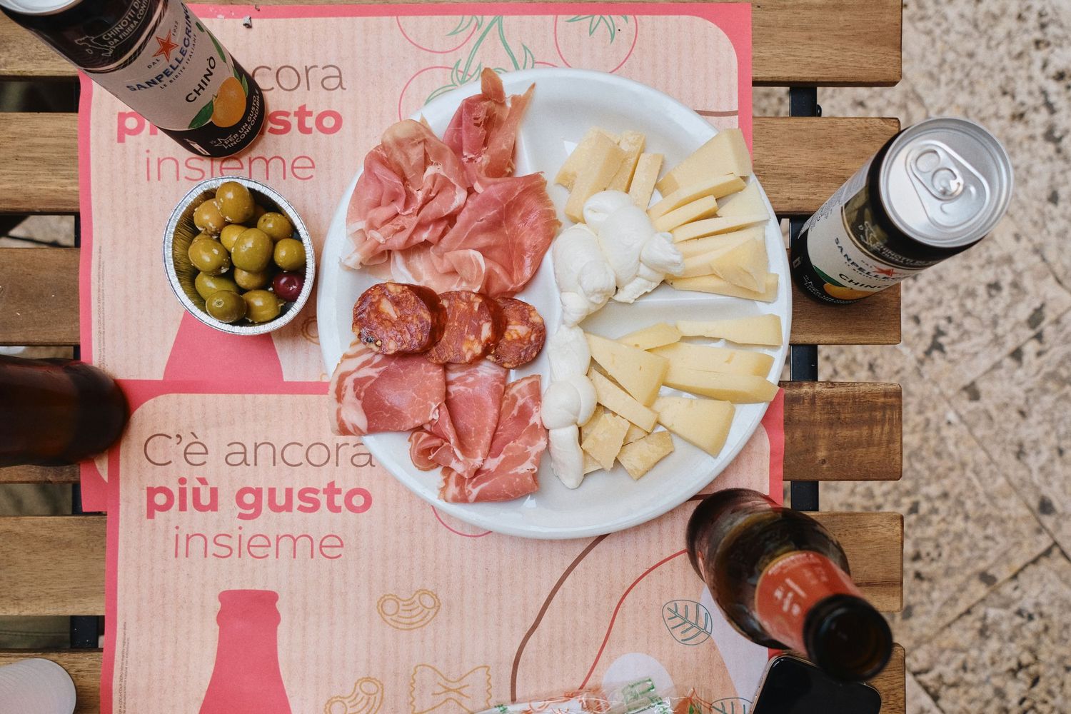 Appetizer plate with cured meats, cheese and olives on pink placemat with drinks.