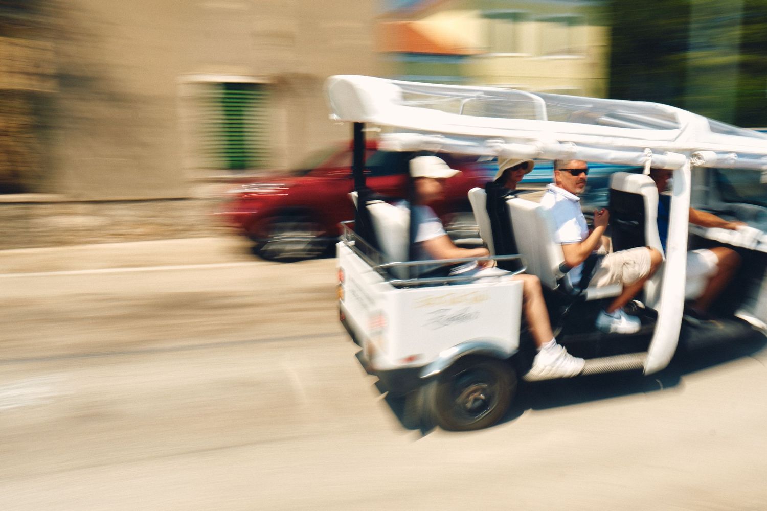 Blurred motion shot of a white golf cart driving on a street.