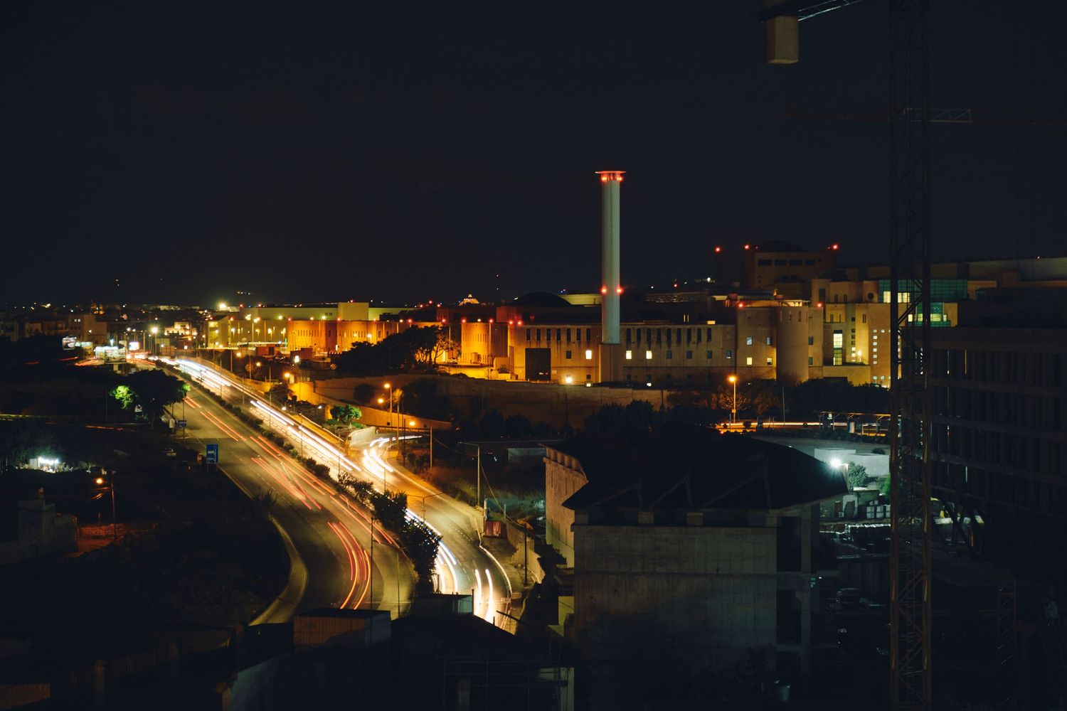 Illuminated coastal cityscape at night with bright lights along the waterfront.
