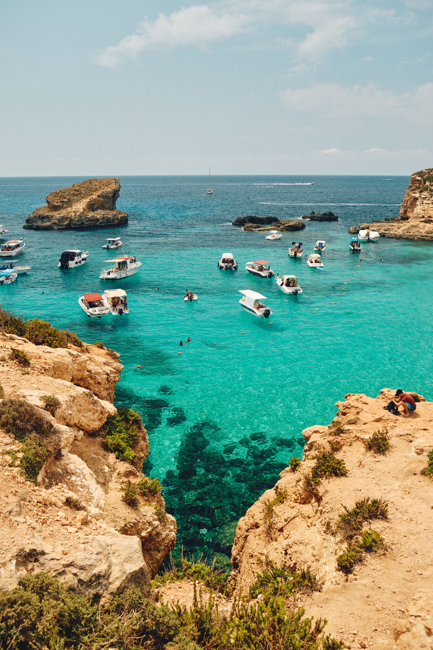 Aerial view of boats anchored in turquoise waters between rocky cliffs in Malta's Blue Lagoon.
