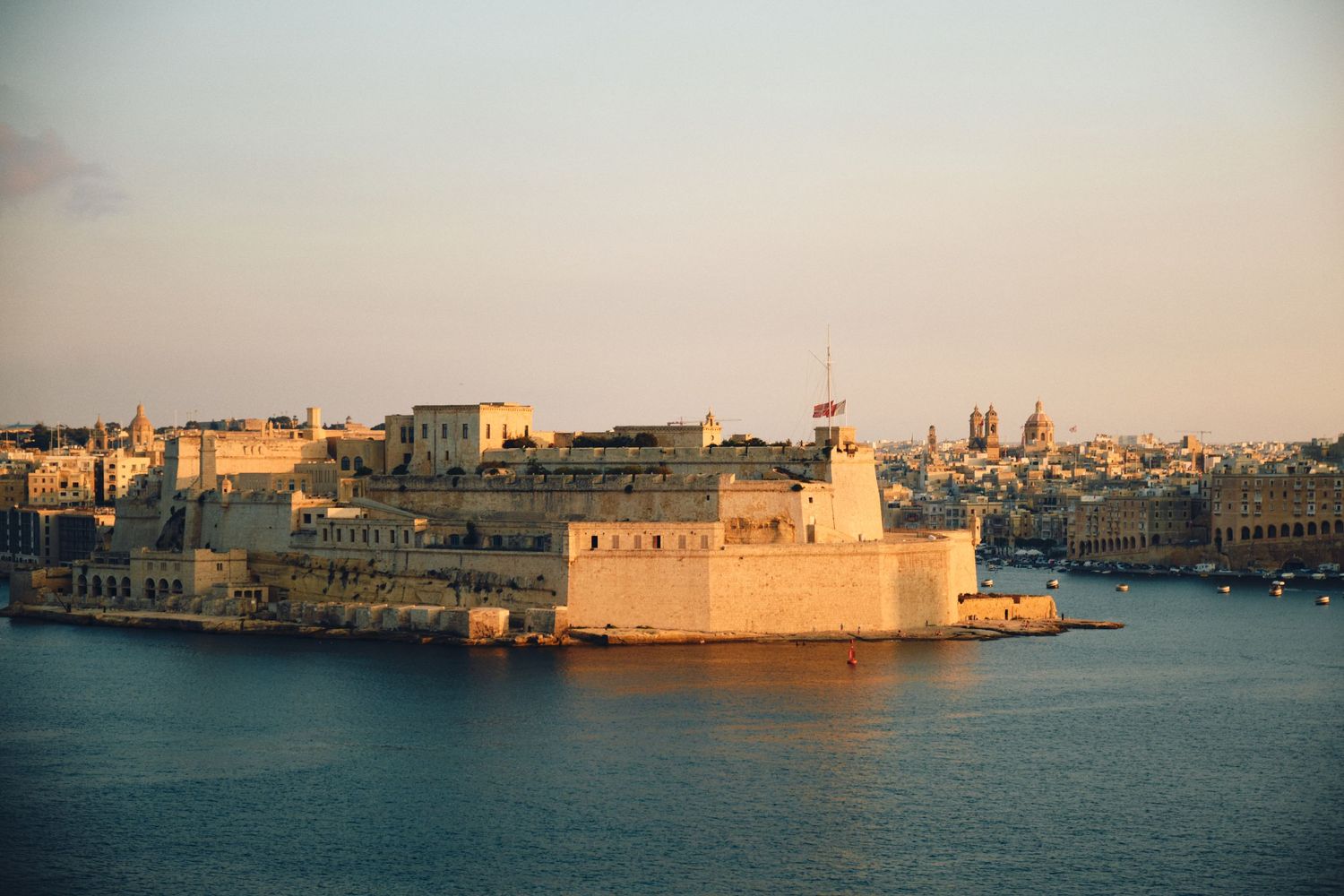 Fort Saint Angelo fortress in Valletta harbor at sunset with warm golden light.