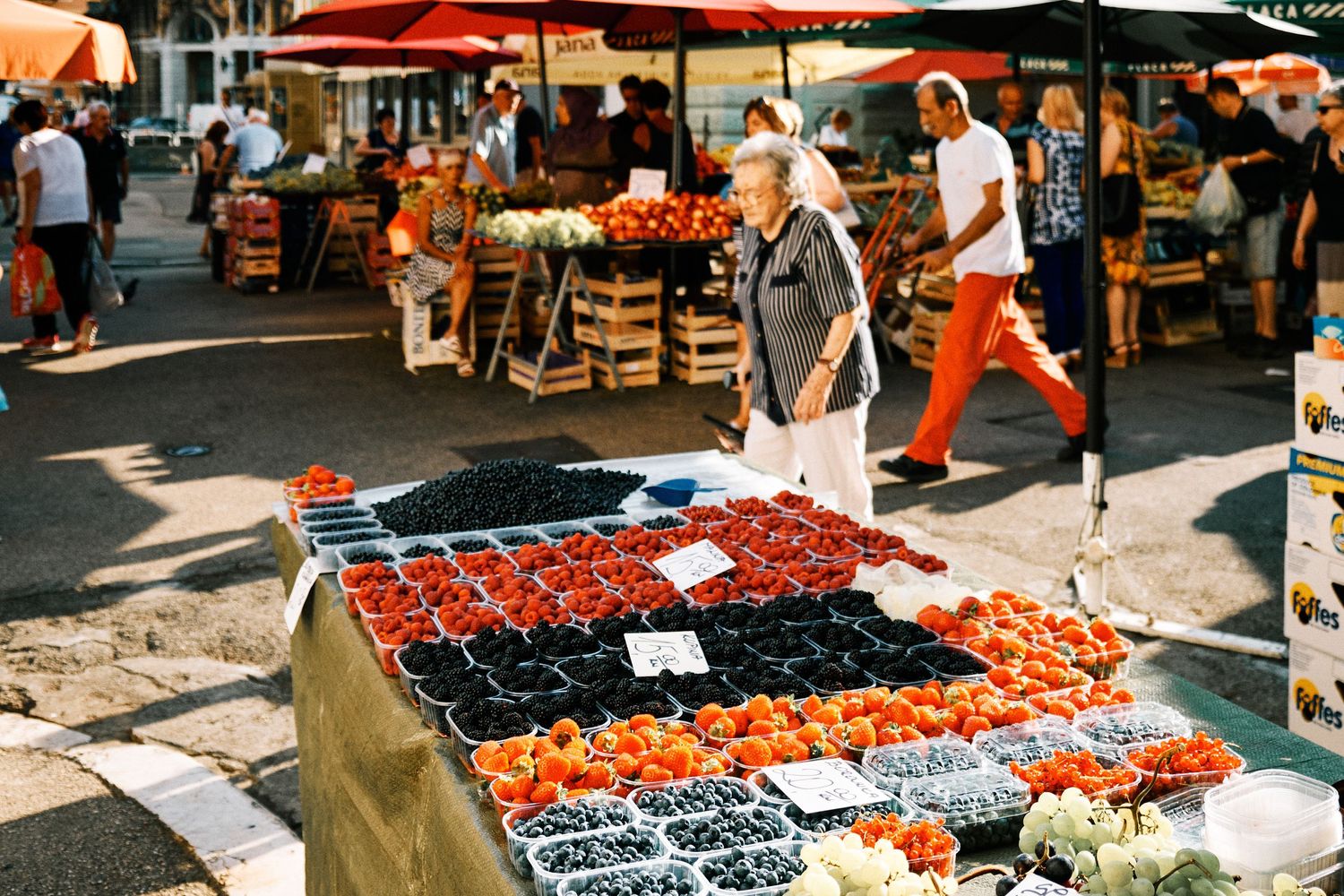 Fresh berries and fruits arranged at an outdoor market stall under red awnings.