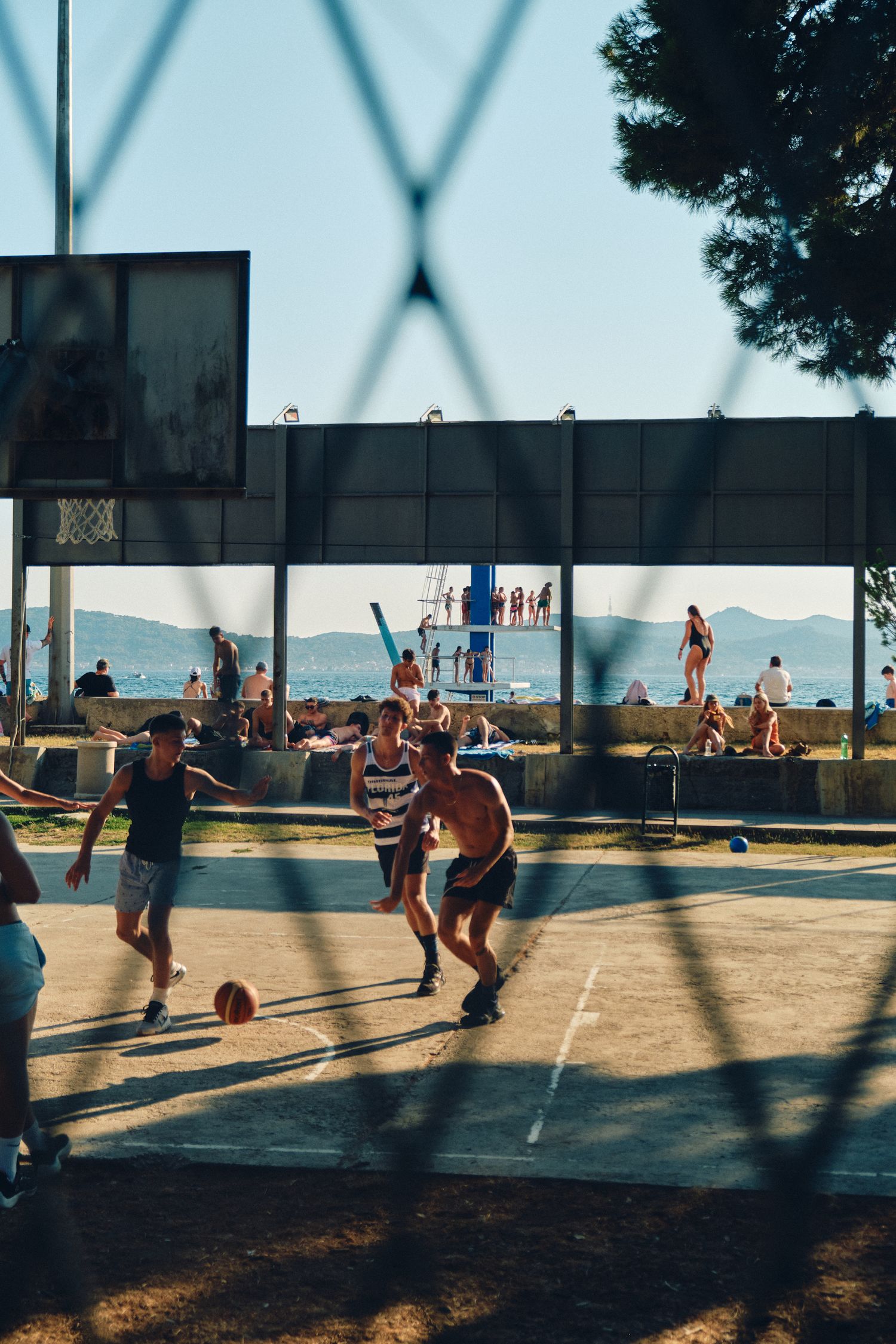 People playing basketball on an outdoor court with mountains visible in the background during sunset.