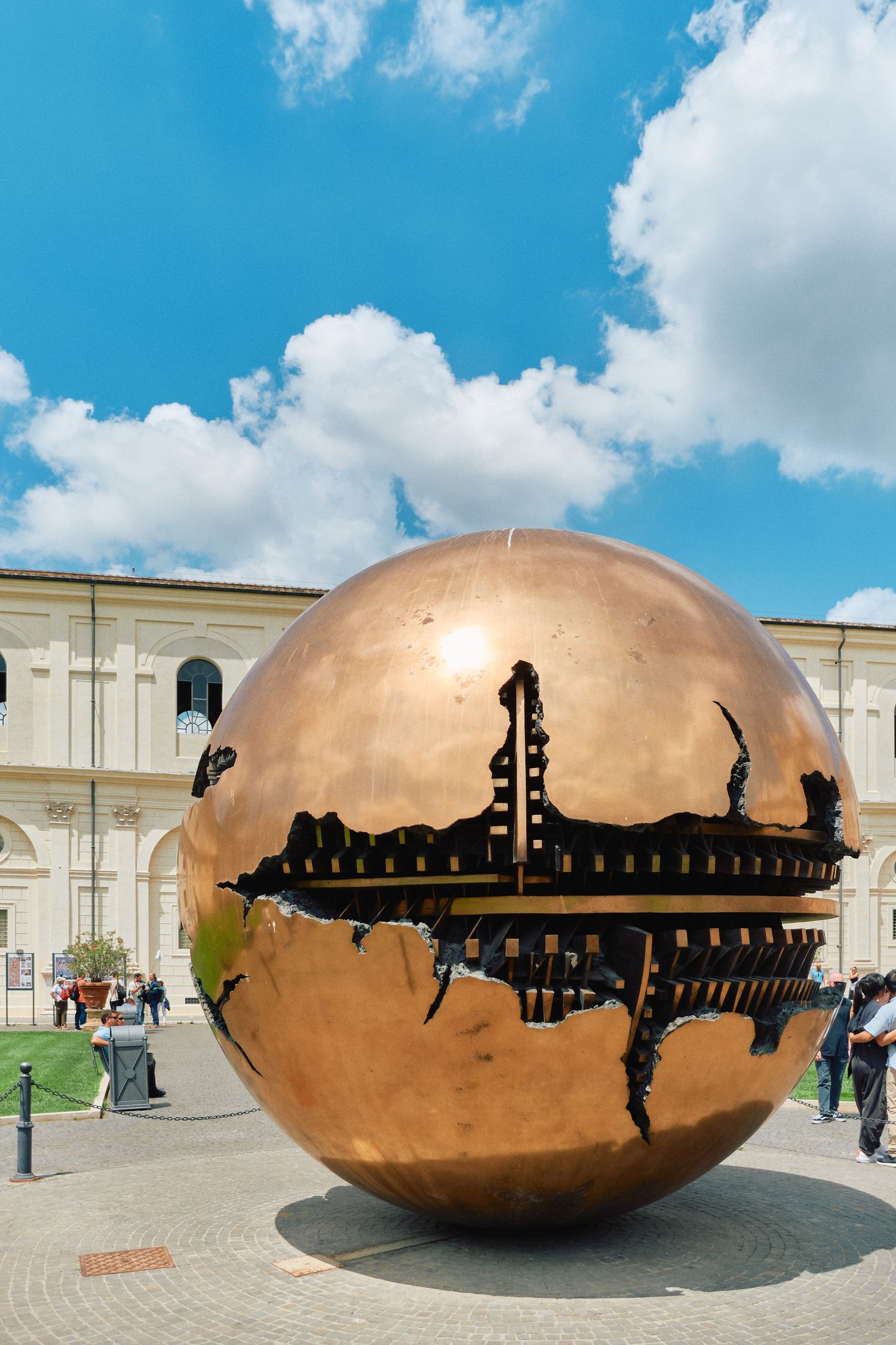 Large spherical bronze sculpture with intricate cutout designs in a courtyard setting.