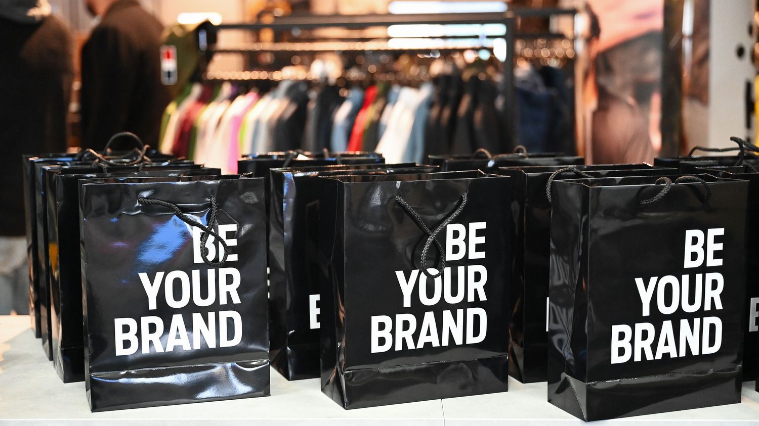 Row of black leather bags with 'YOUR BRAND' text displayed on retail store shelves.