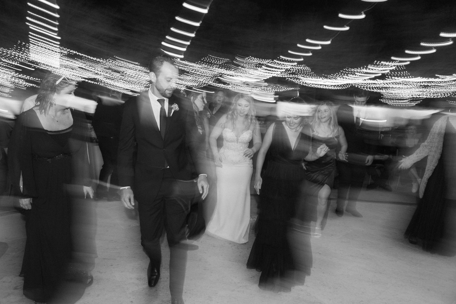 Motion-blurred black and white photograph of people dancing at a formal event with overhead lights creating streaks of light in Moorpark.