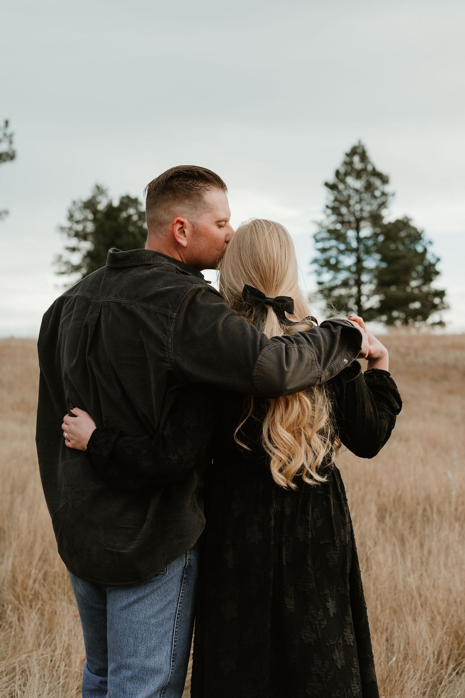 A couple sharing an intimate moment in a field of tall grass during an overcast day.