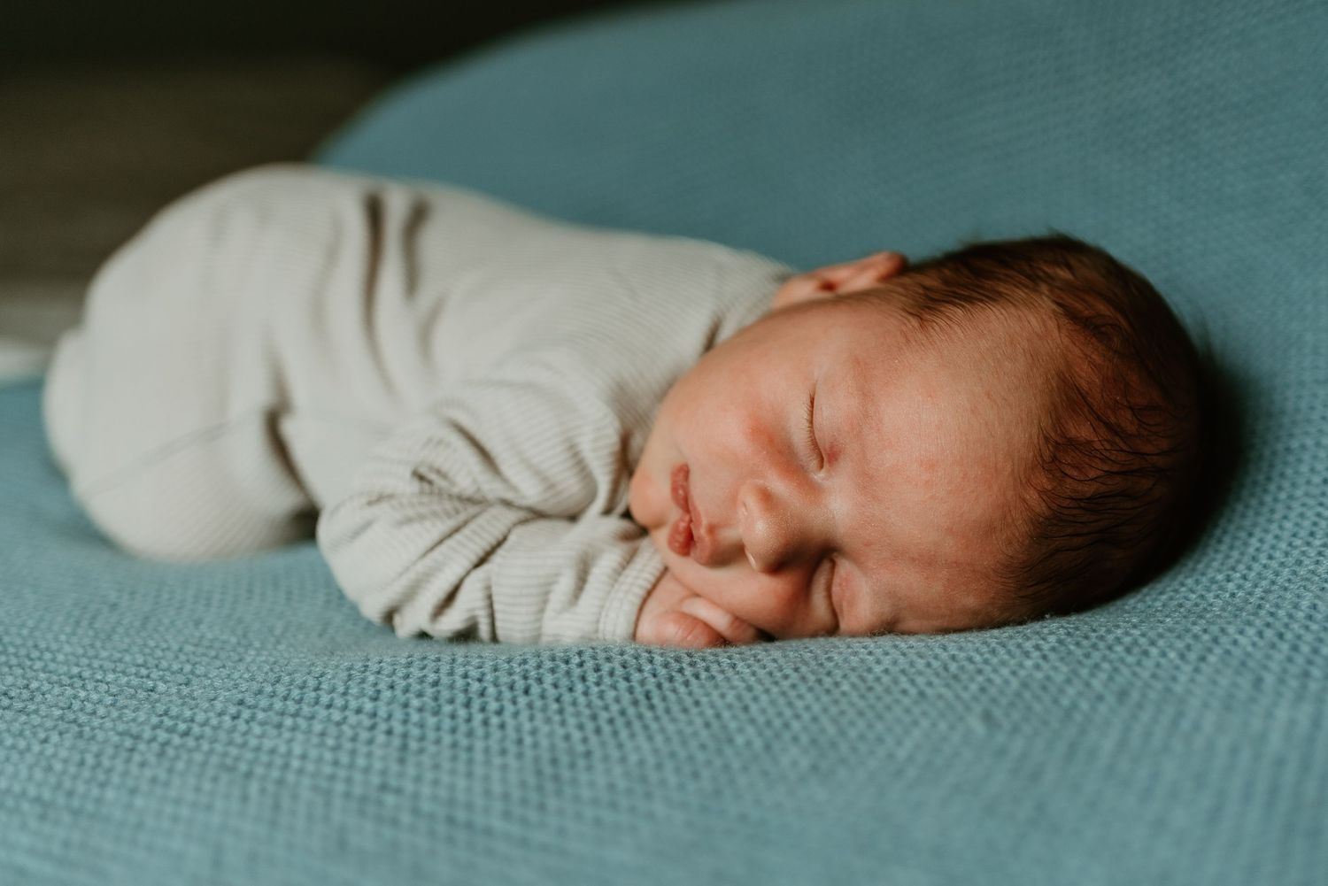 A sleeping newborn baby wrapped in white swaddle lies peacefully on a teal textured blanket.