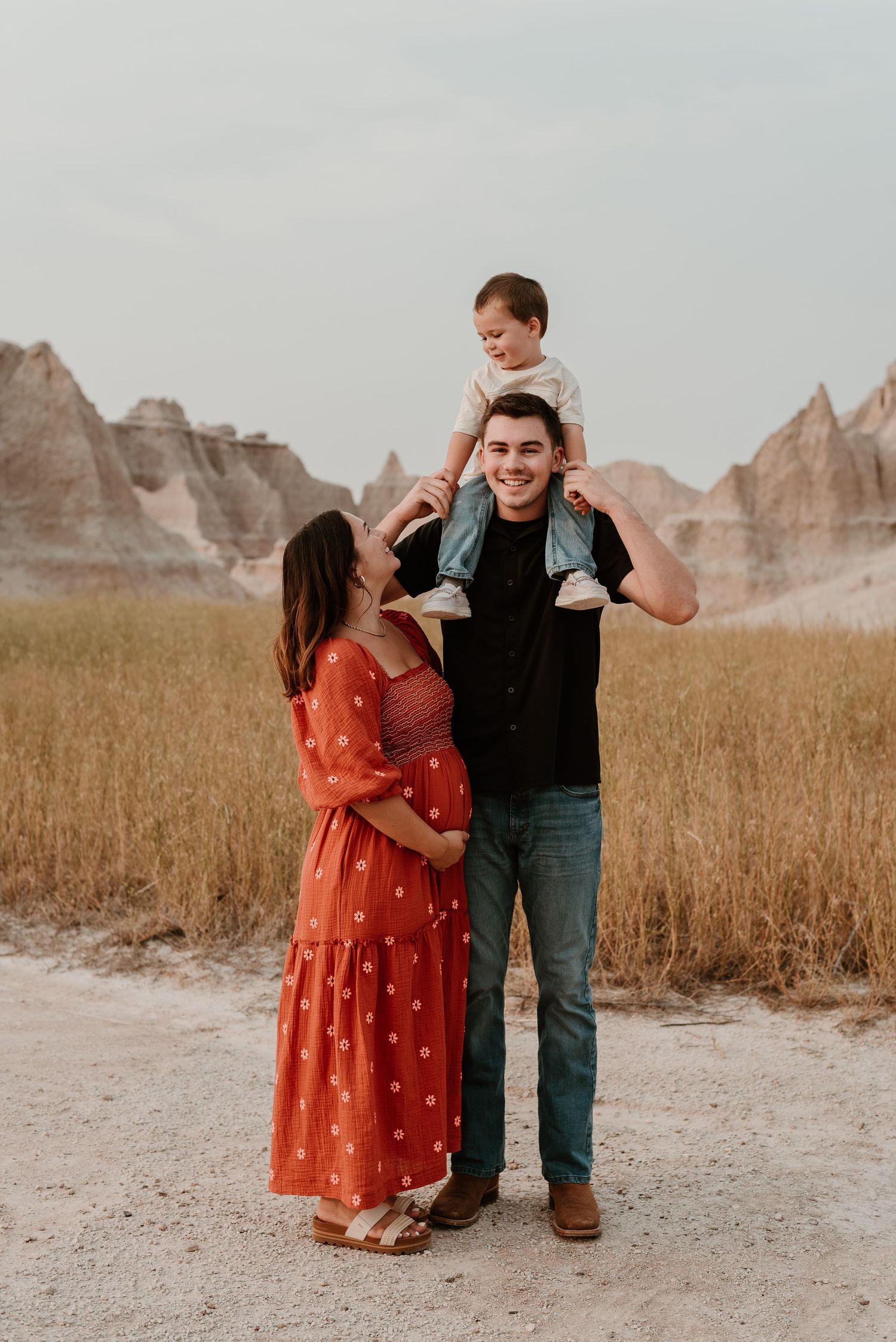 A family takes playful photos together against a backdrop of rugged desert mountains and tall grass.