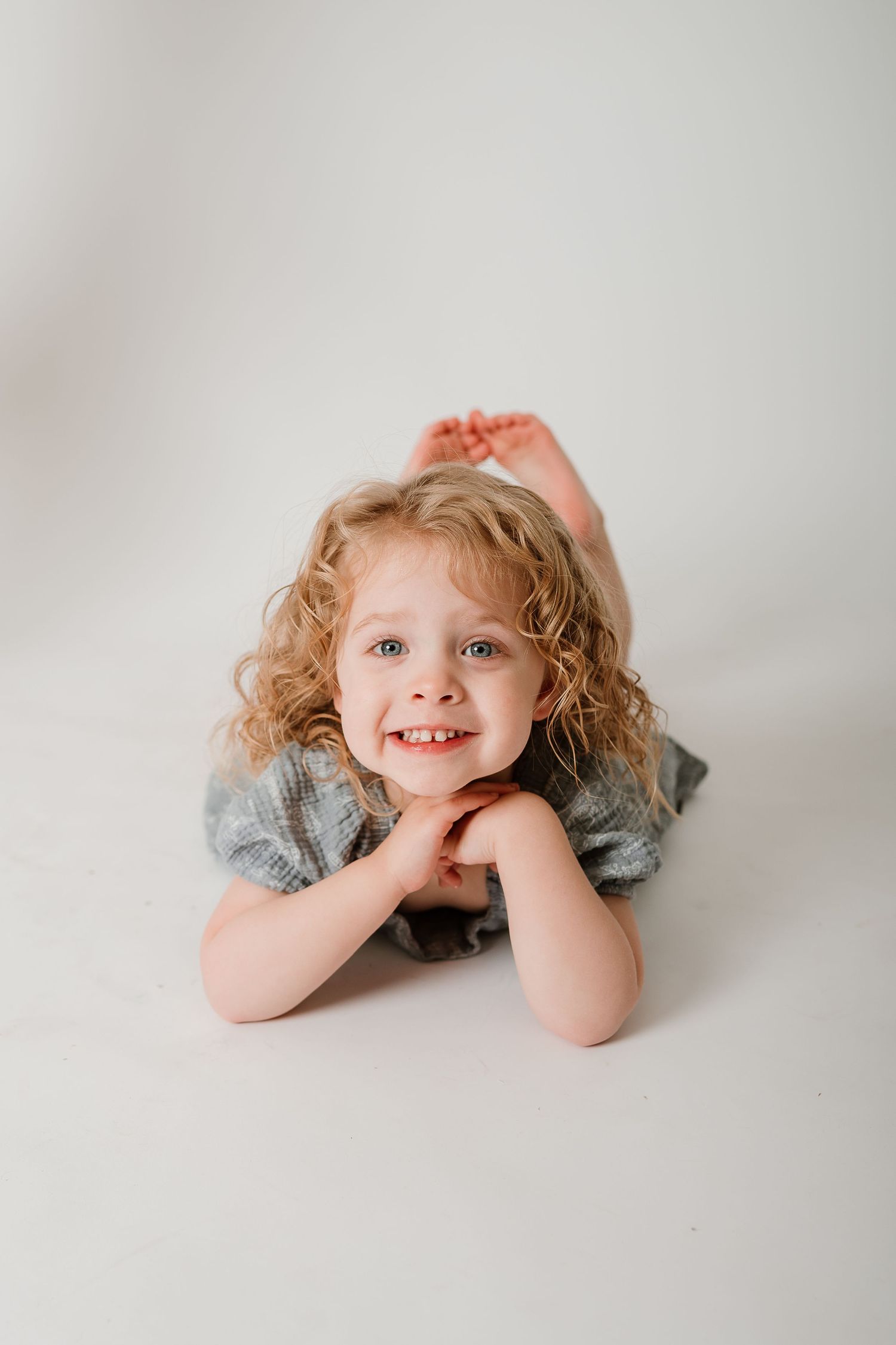 A series of four minimalist portraits showing a child lying down on a light gray background in different playful poses.