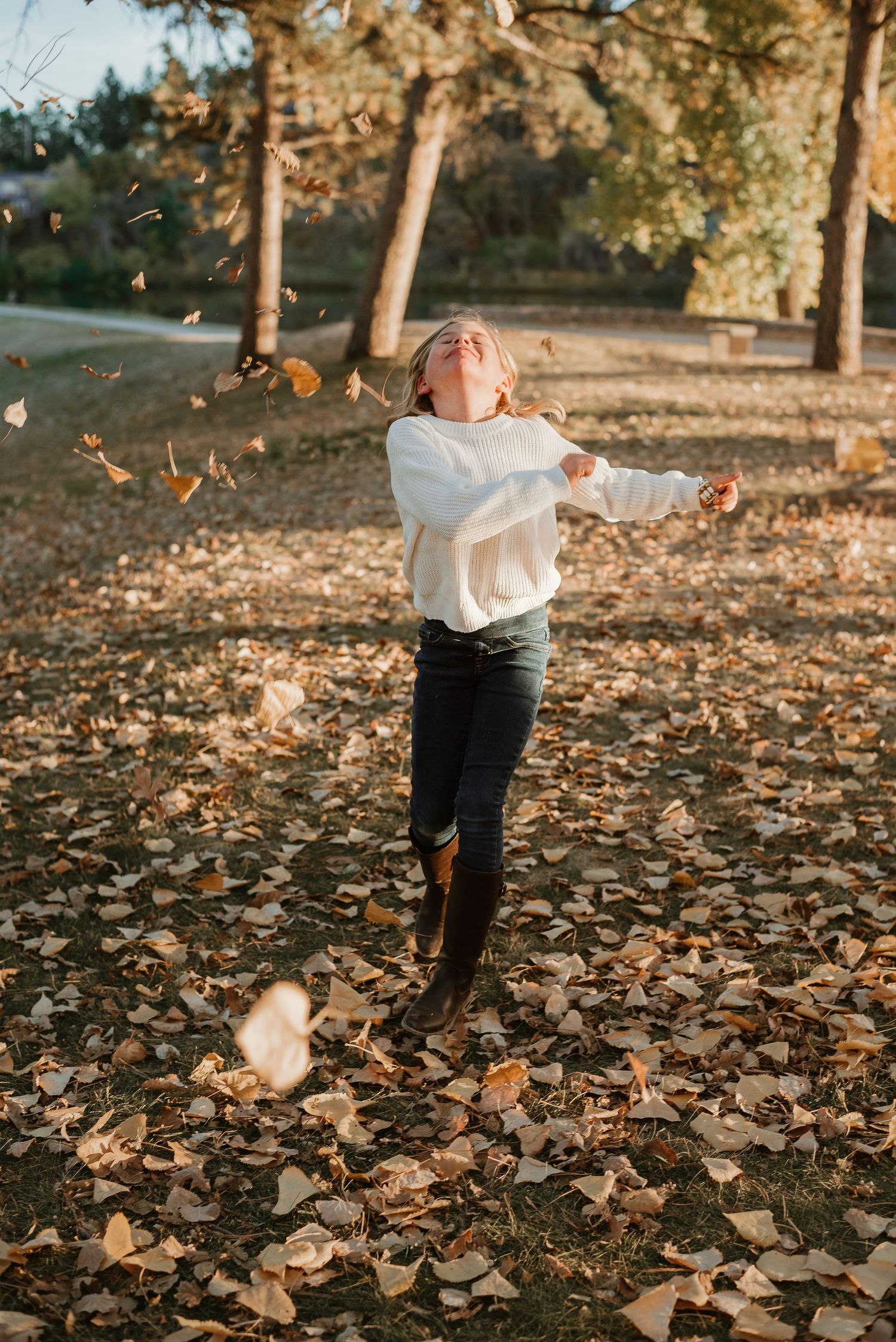 Autumn leaves scatter in the air as someone plays in a park filled with fallen foliage.