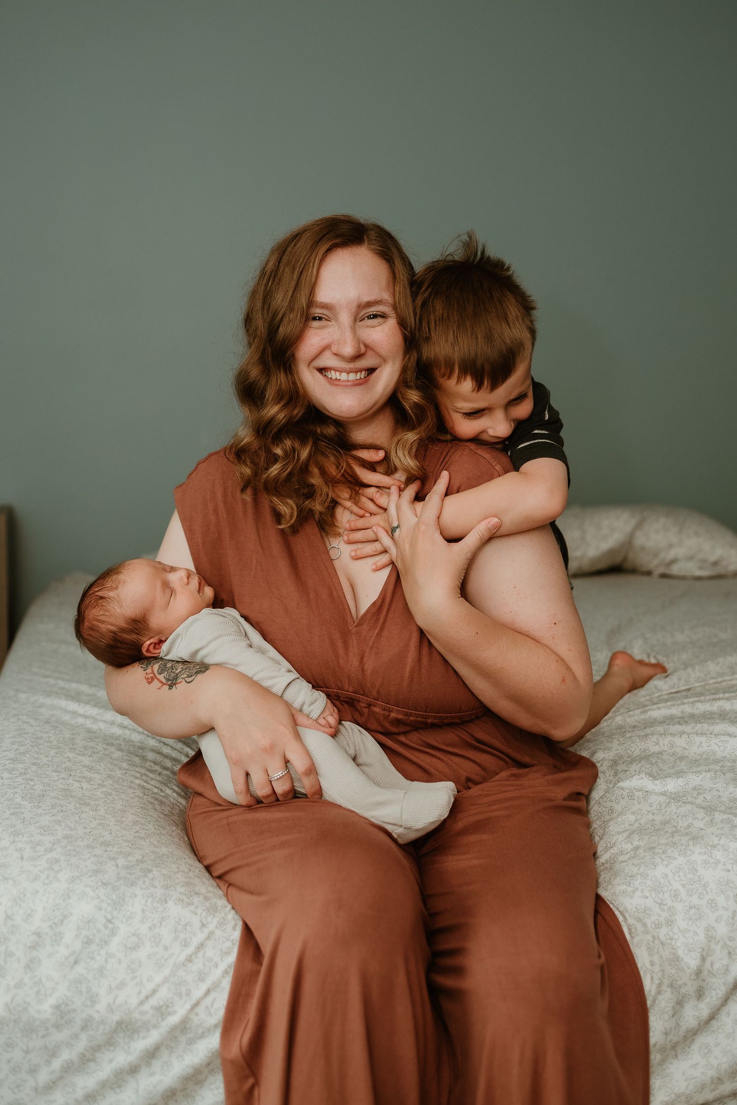 Family members share joyful moments together on a bed with soft green wall backdrop.
