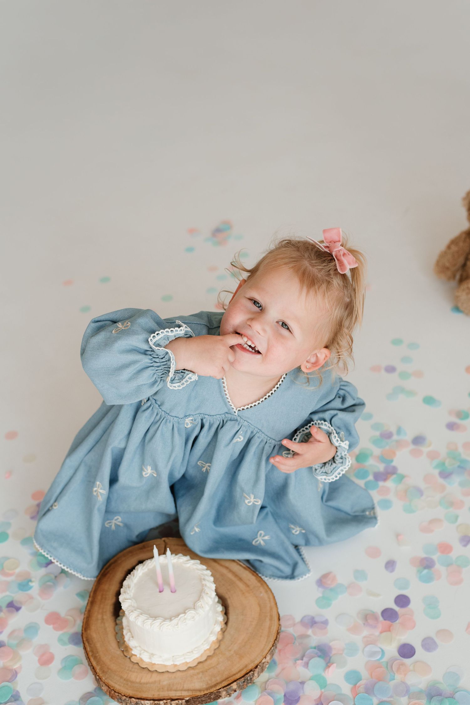 A cake smash photo session featuring a blue dress and confetti scattered on a white backdrop.