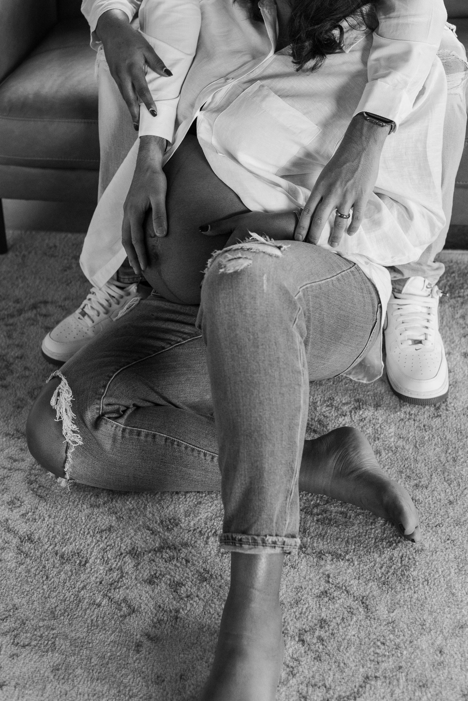 Black and white photo showing intimate moment on couch with distressed denim and white shirt.