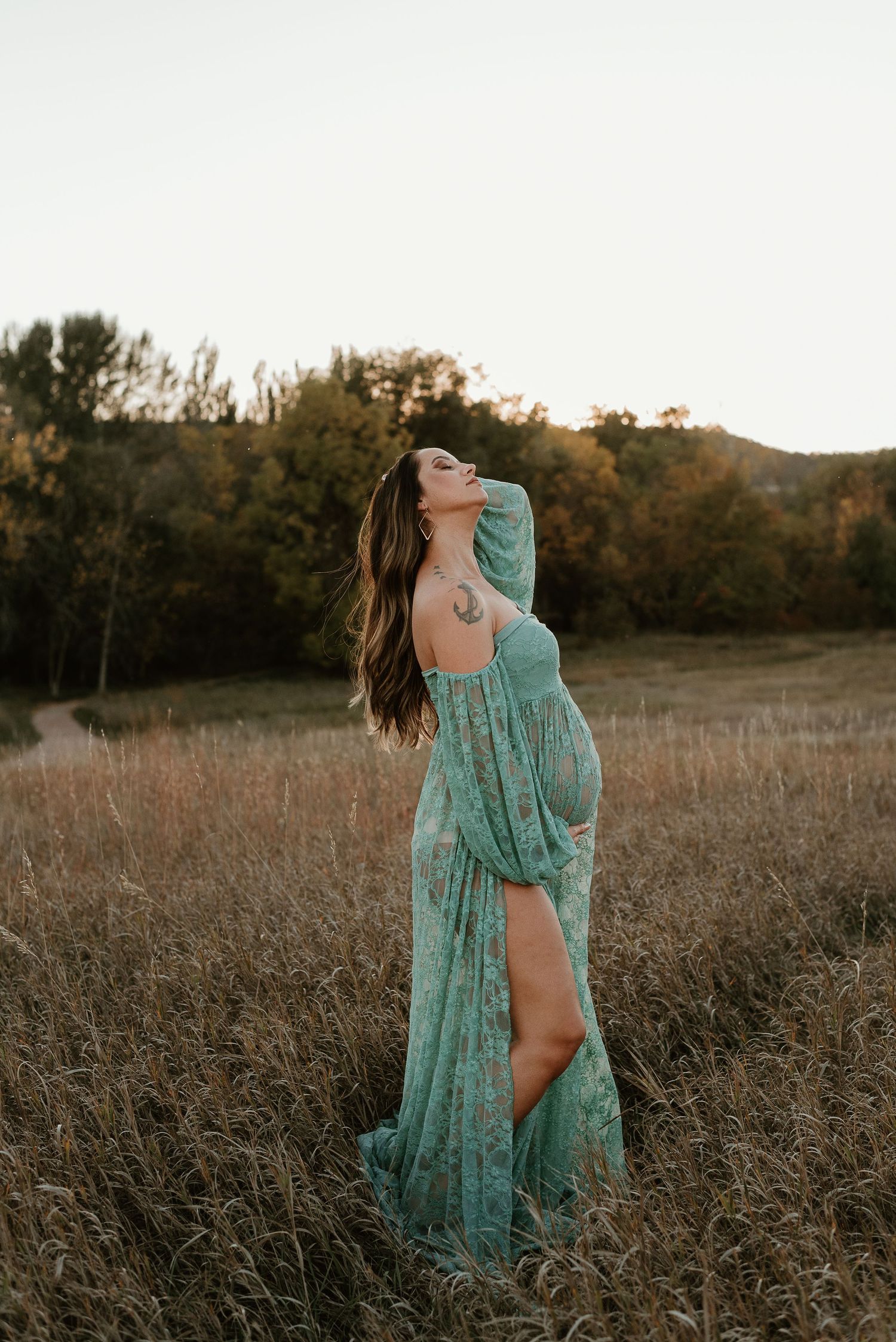 Woman in flowing turquoise dress poses gracefully in a golden field at sunset.