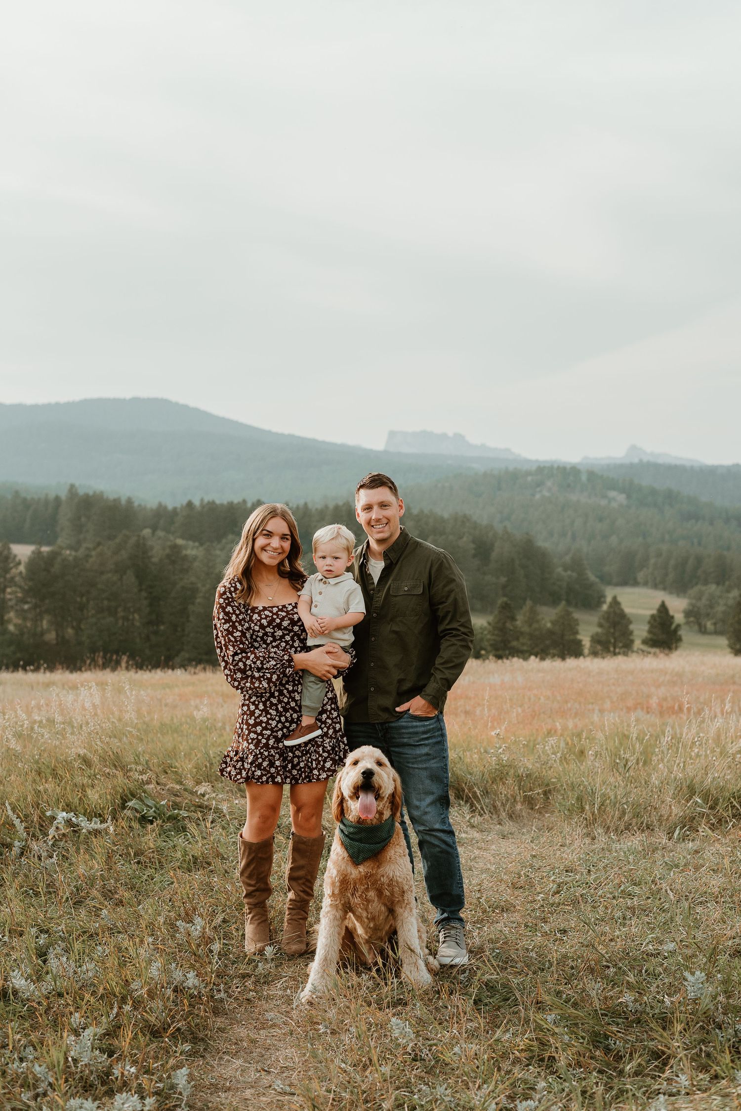 A family and their dog pose together in a scenic mountain meadow during an outdoor photo session.