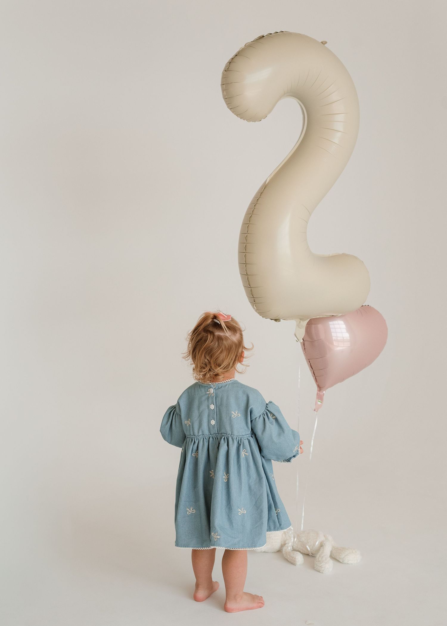 A second birthday photoshoot setup with cream-colored number balloons and blue dress.