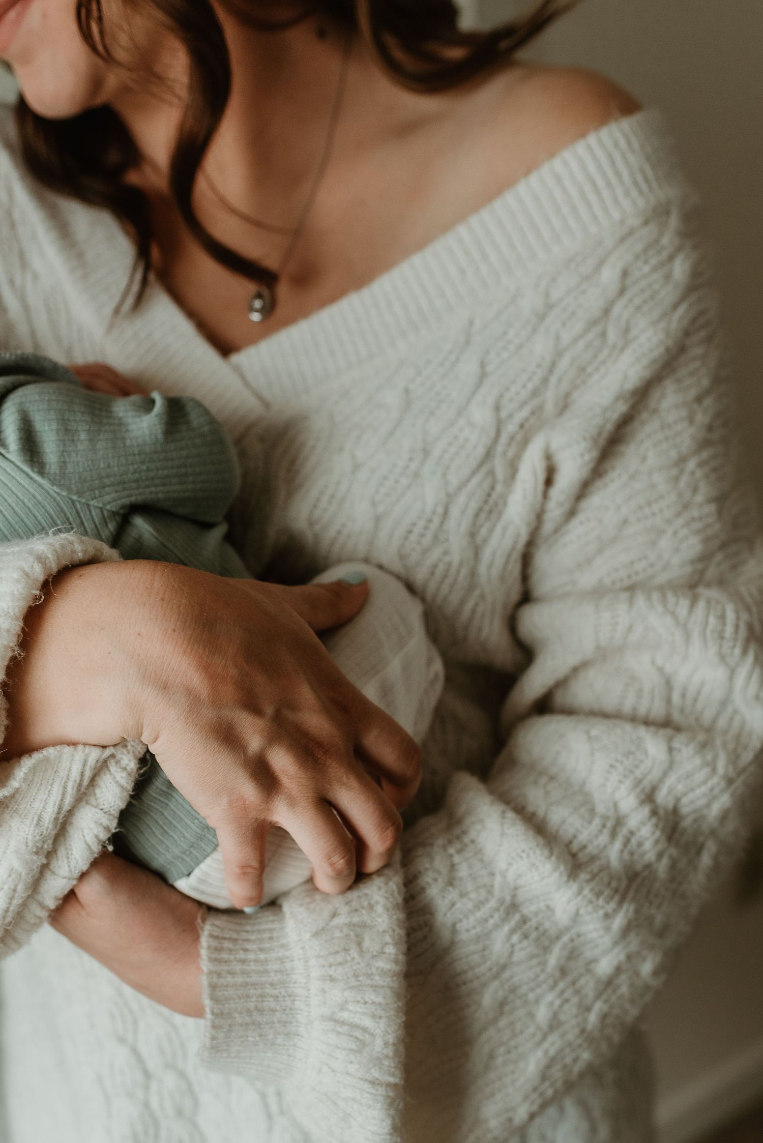 A person in a cable knit sweater holds a baby in soft, intimate lighting.