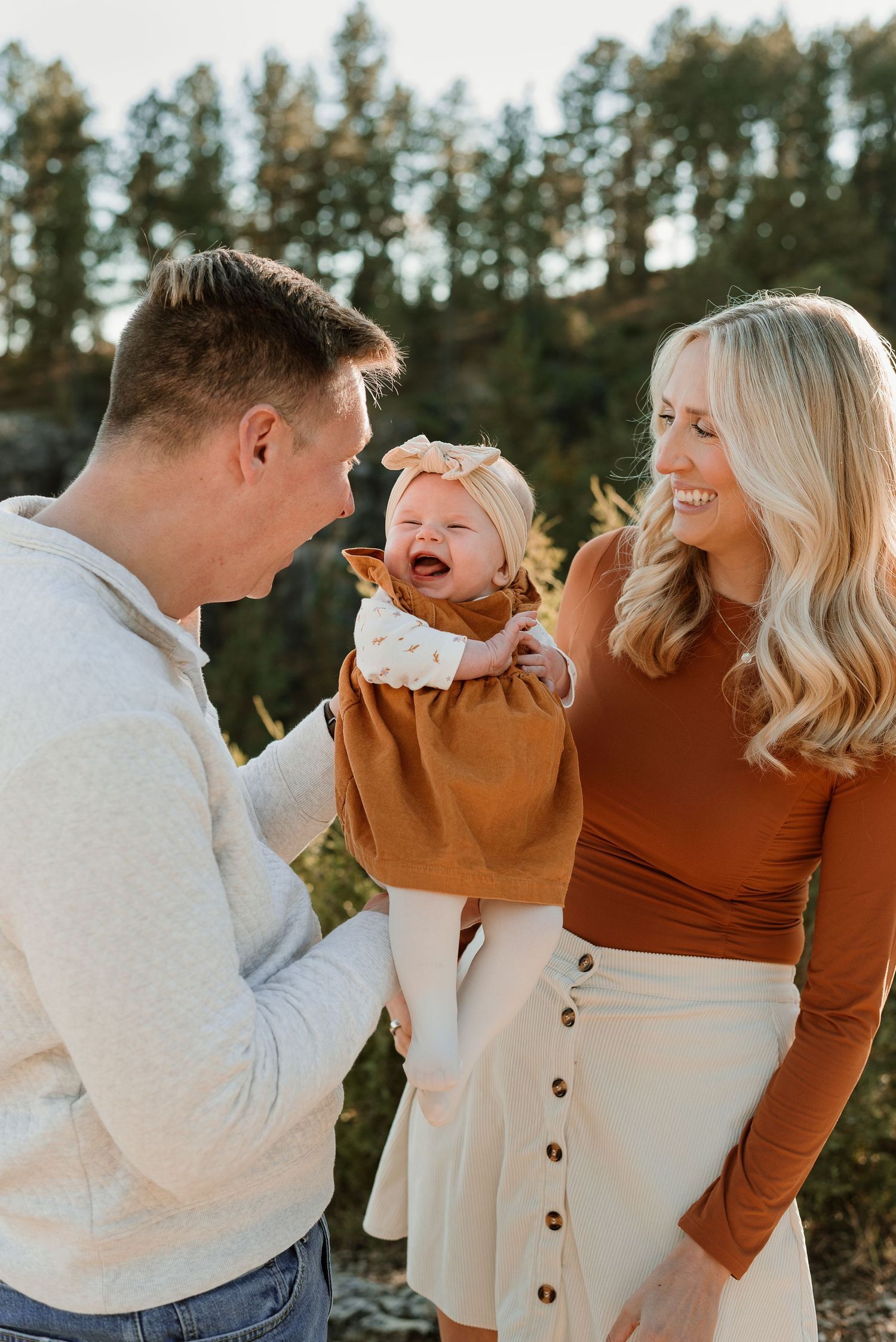 Couple laughing together during outdoor photo session wearing brown and cream colored outfits.