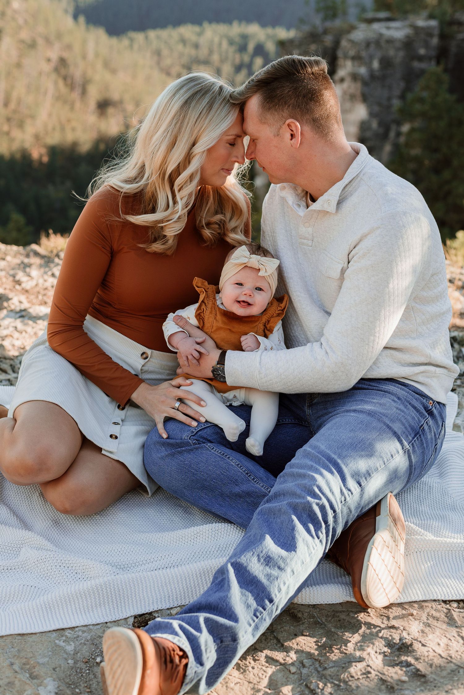 Family lying on white blanket outdoors sharing tender moments together in natural lighting.