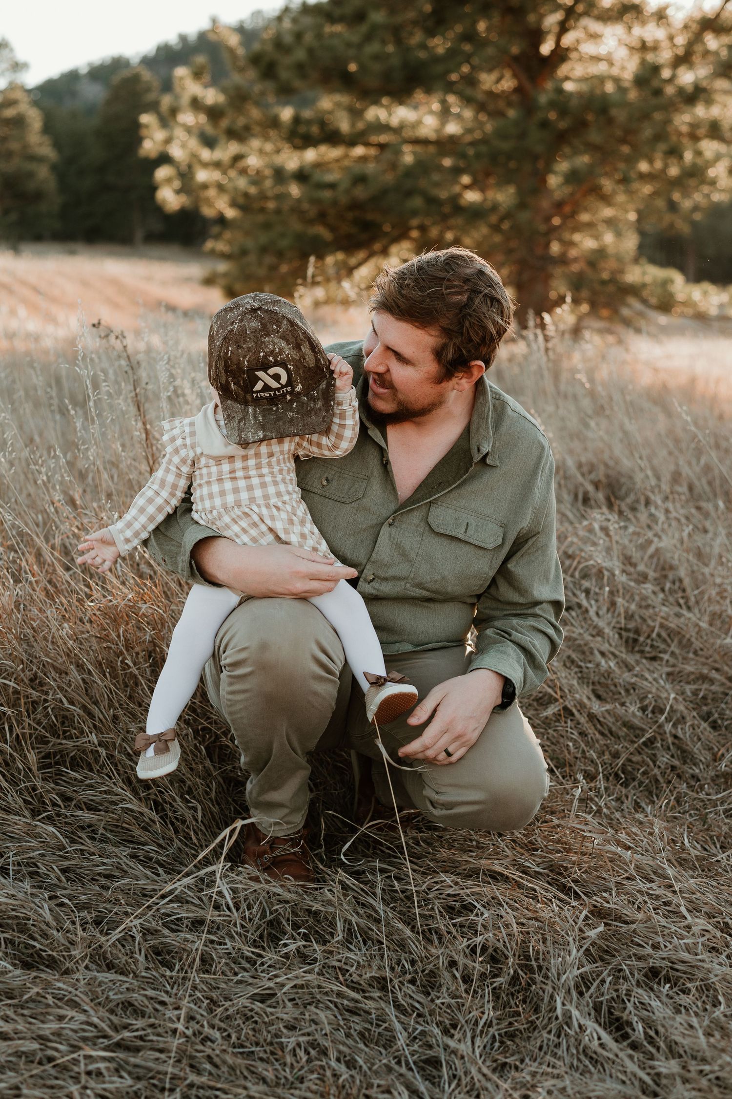 A tender moment between parent and child sitting in tall grass during golden hour sunset in a rural field.