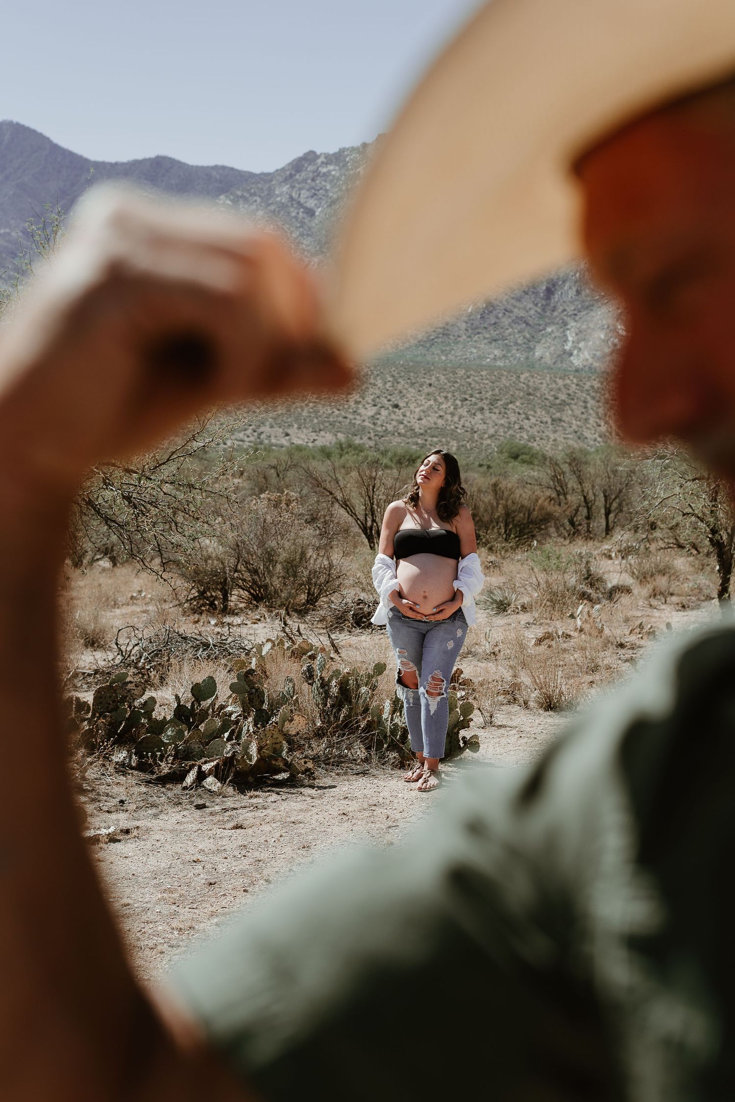 Desert maternity photo session with mountains and cacti in soft focus.